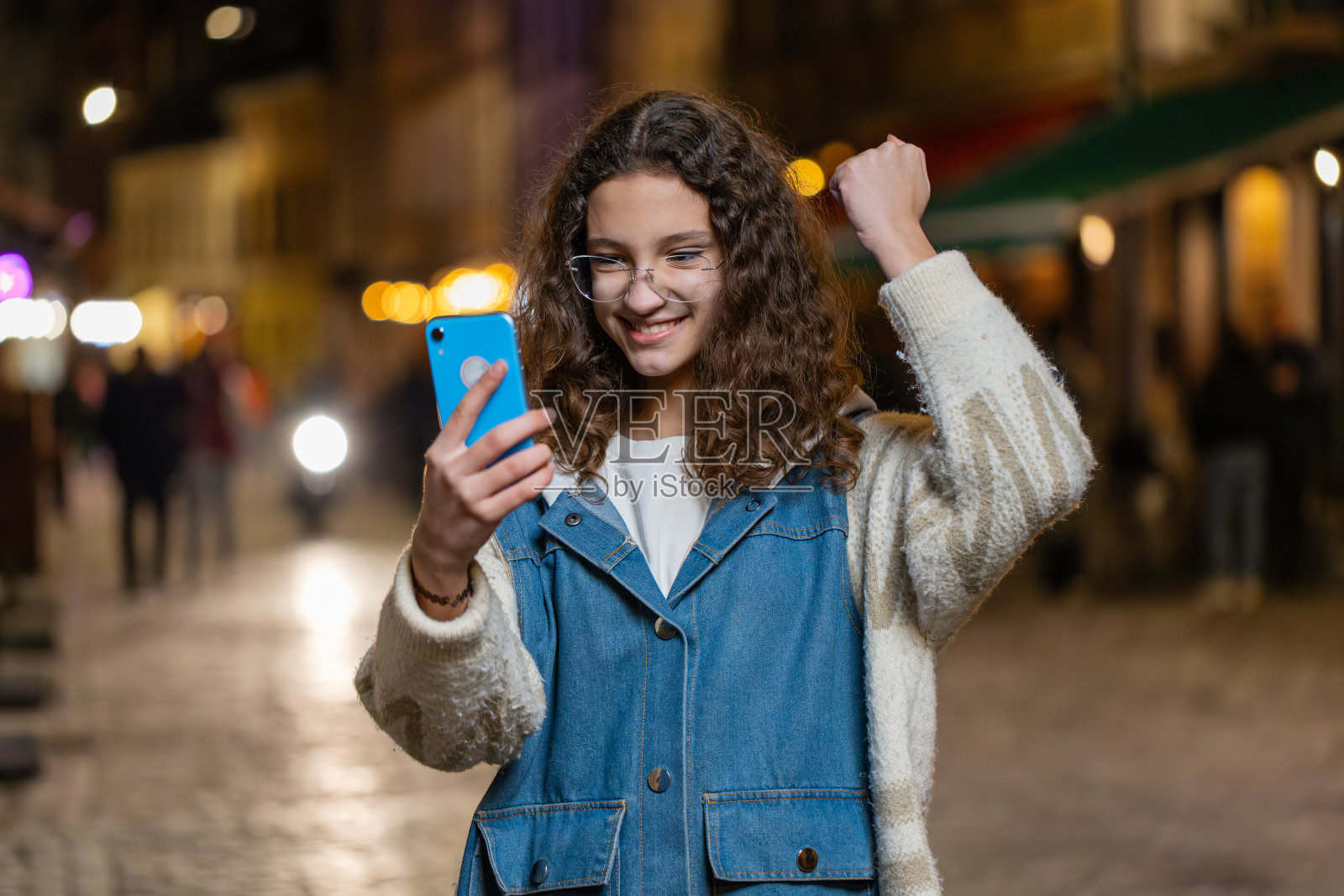 在城市夜晚的街道上，女孩用智能手机庆祝赢得好消息消息彩票头奖照片摄影图片