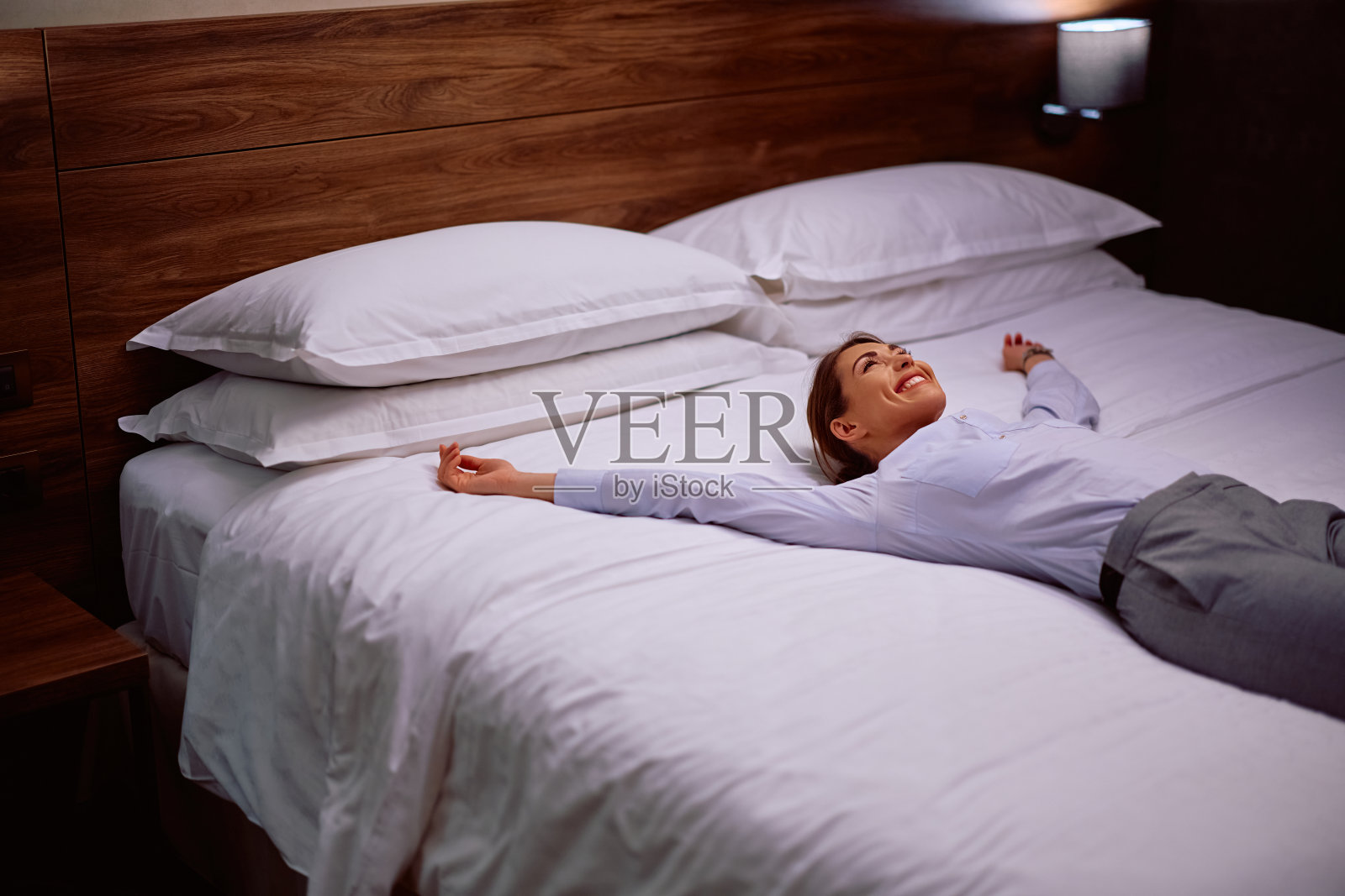 年轻快乐的女商人到达酒店后躺在床上休息。照片摄影图片