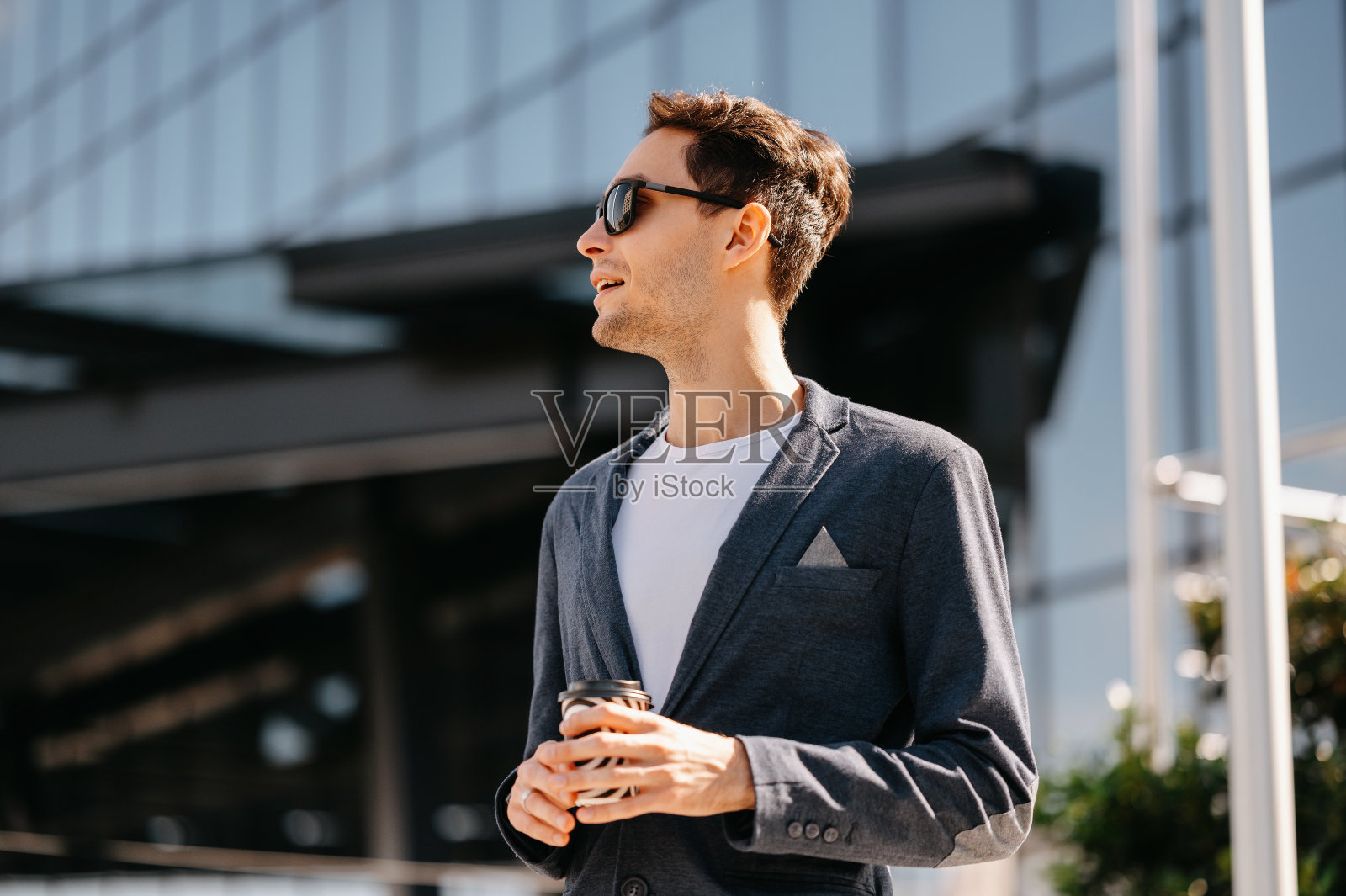 穿着夹克的英俊年轻人拿着咖啡杯向一边看。照片摄影图片