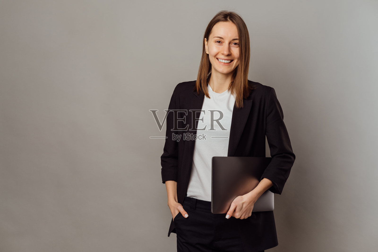 一个穿着西装，腋下夹着笔记本电脑的快乐女人的工作室肖像。照片摄影图片