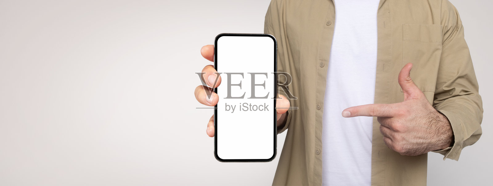 身穿卡其色衬衫和白色t恤的男子手持智能手机，屏幕朝前照片摄影图片