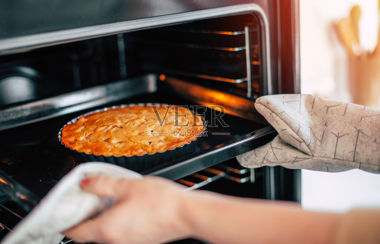 一名妇女用厨房手套从厨房的烤箱中取出自制的甜点苹果素派。照片摄影图片