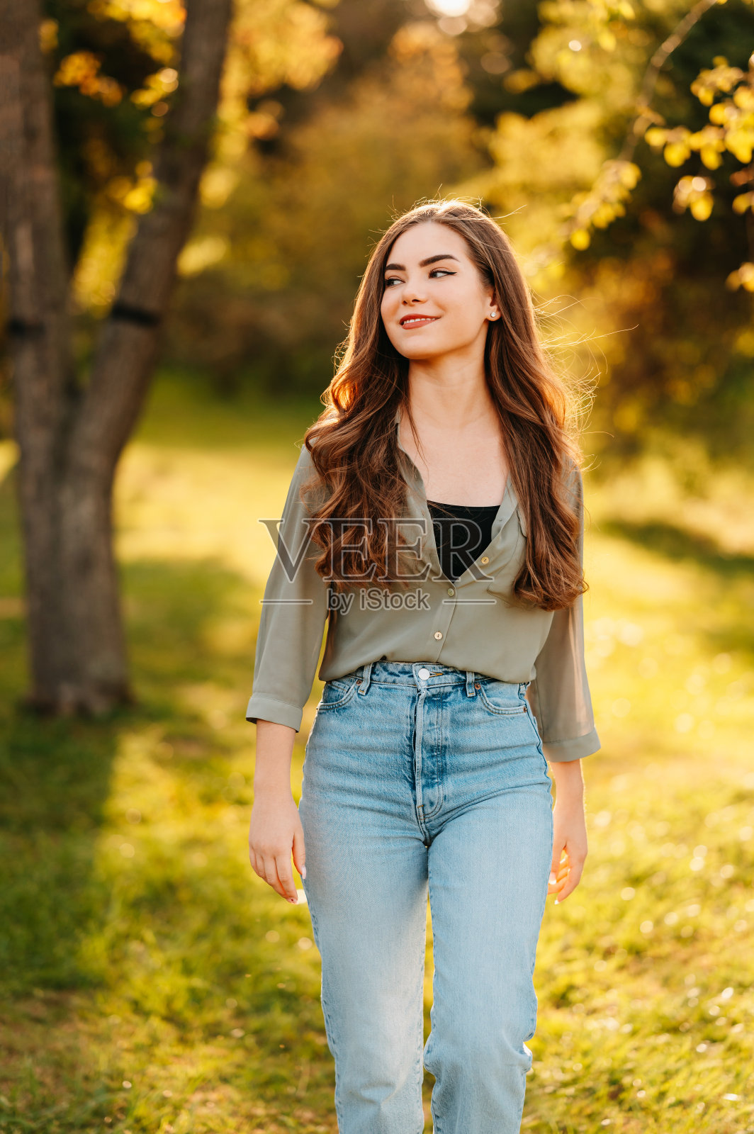 一个阳光明媚的日子里，一个年轻女子在公园散步的垂直户外照片。照片摄影图片