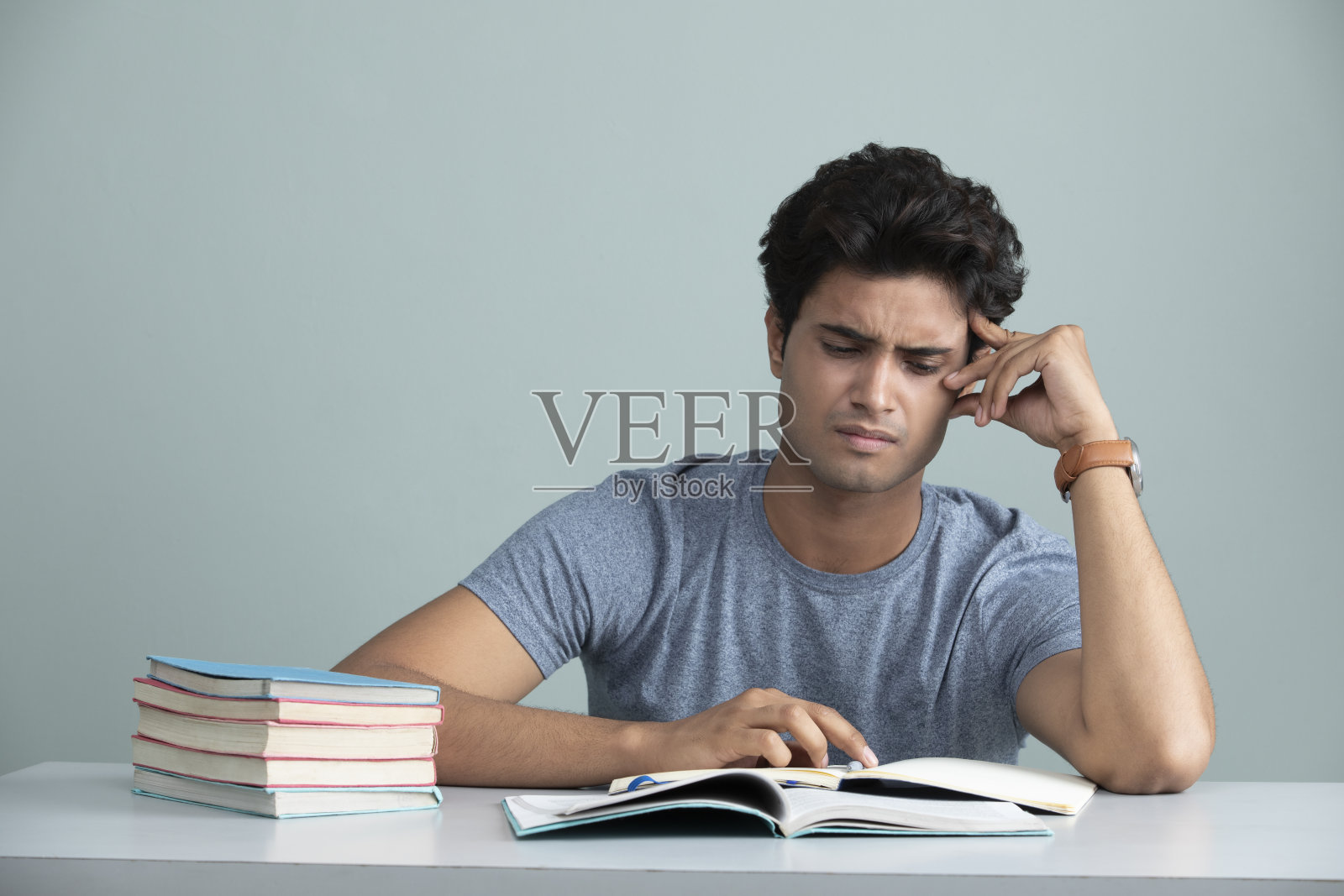 年轻疲惫的学生在书桌上看书。照片摄影图片