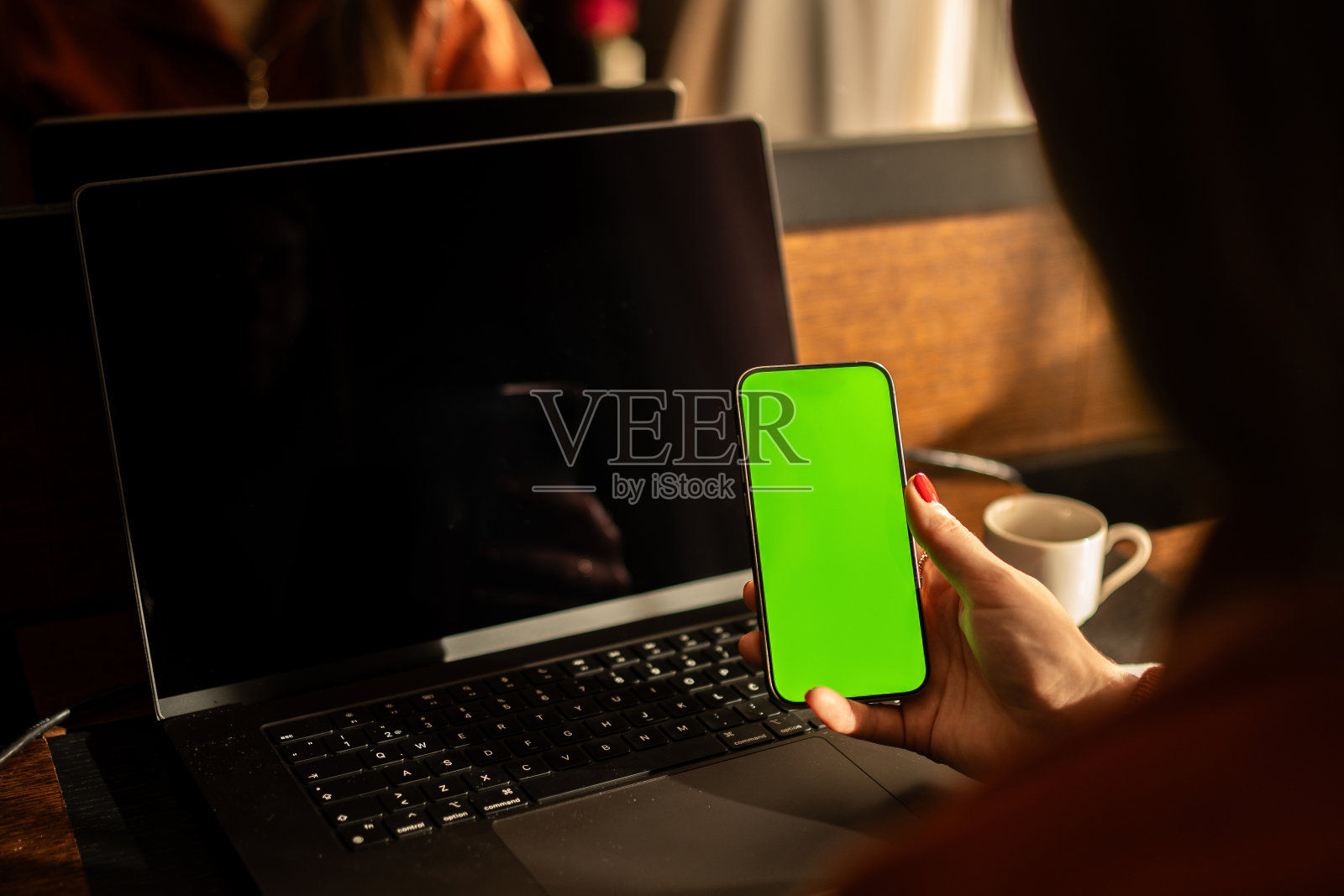 女自由职业者在酒店房间里用手机绿屏在笔记本电脑上工作的后视图照片摄影图片