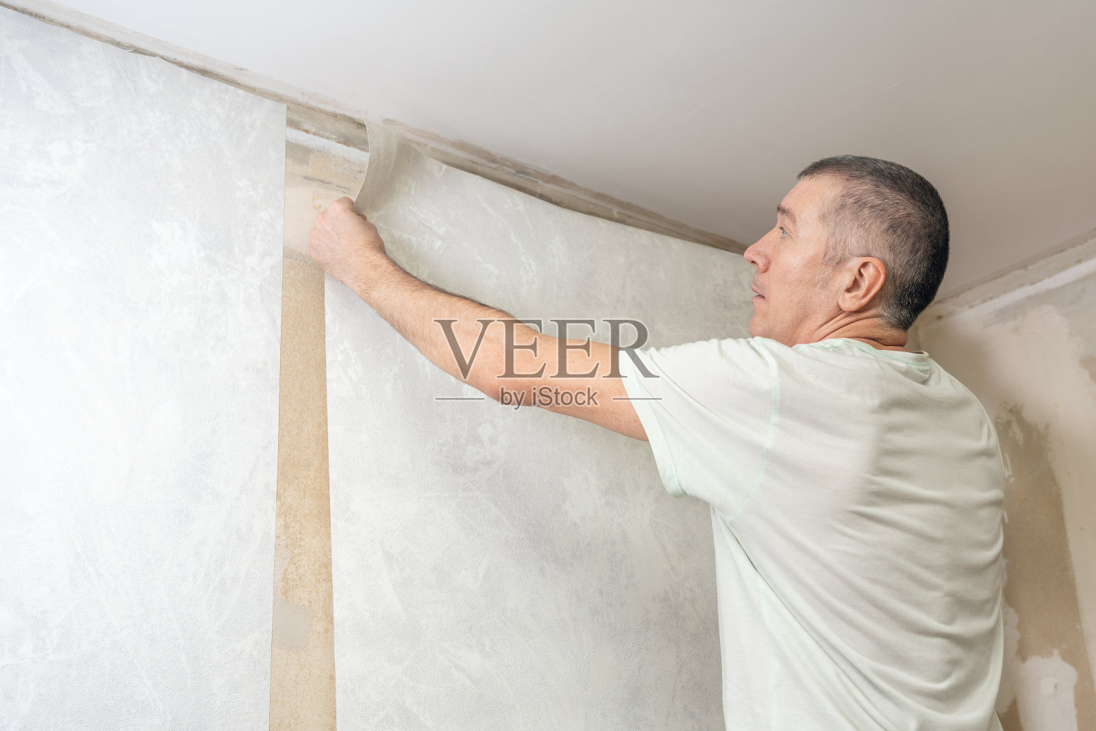 一个男人正在把无纺布墙纸粘在墙上。房间装修照片摄影图片