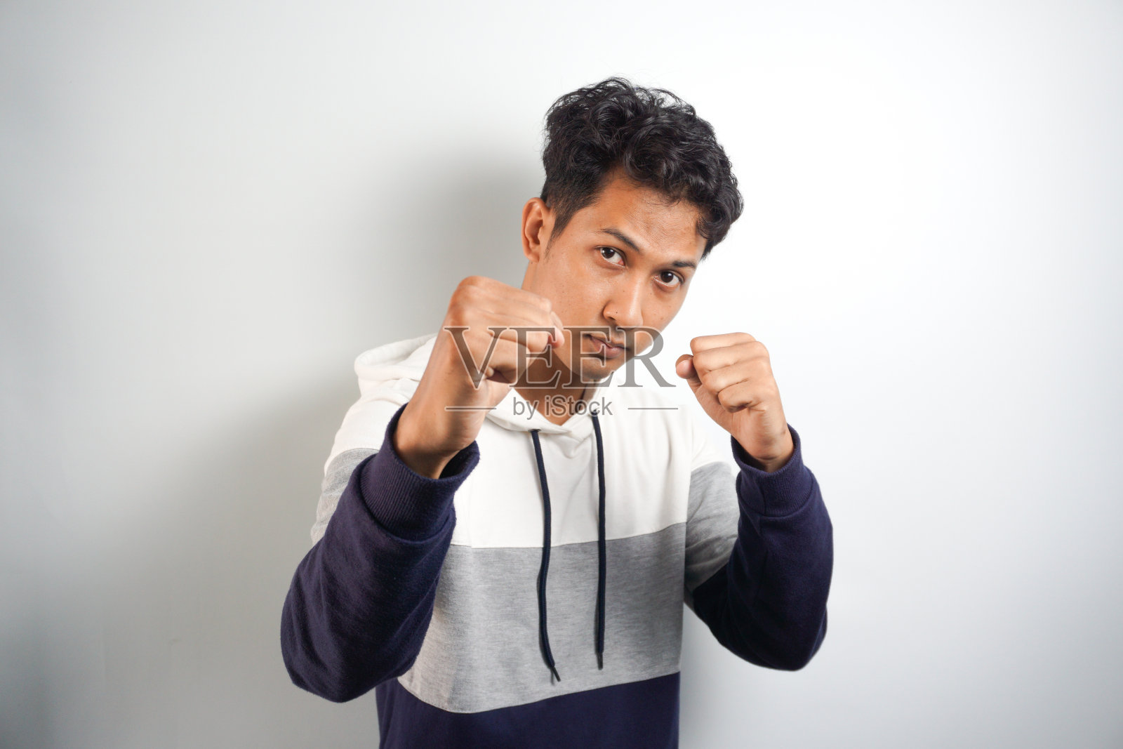 来吧，让我们战斗。图为兴奋、自信、傲慢的男模，在酒吧里举起拳头，摆出拳击手的姿势，想要在白墙上打别人照片摄影图片