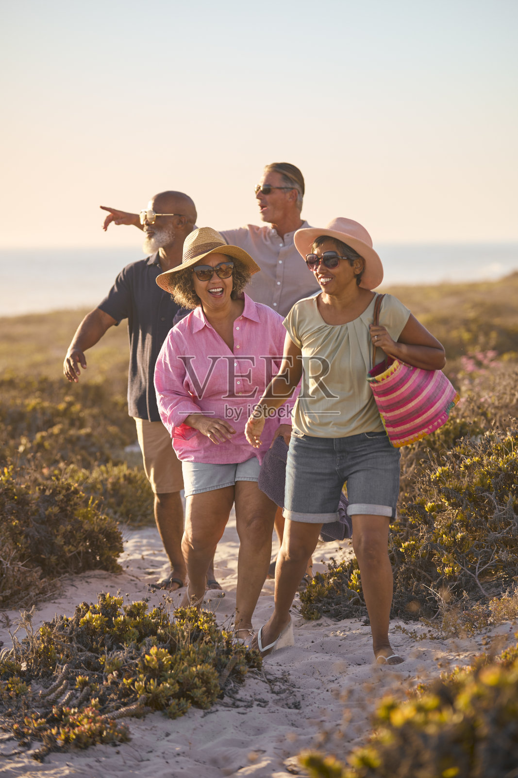一对带着朋友的成熟夫妇在暑假里背着包走在沙滩上的沙丘上照片摄影图片