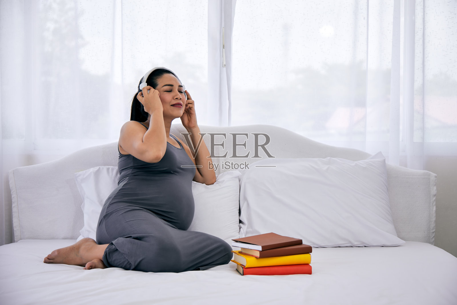孕妇坐在床上，戴着耳机听音乐，面带微笑照片摄影图片