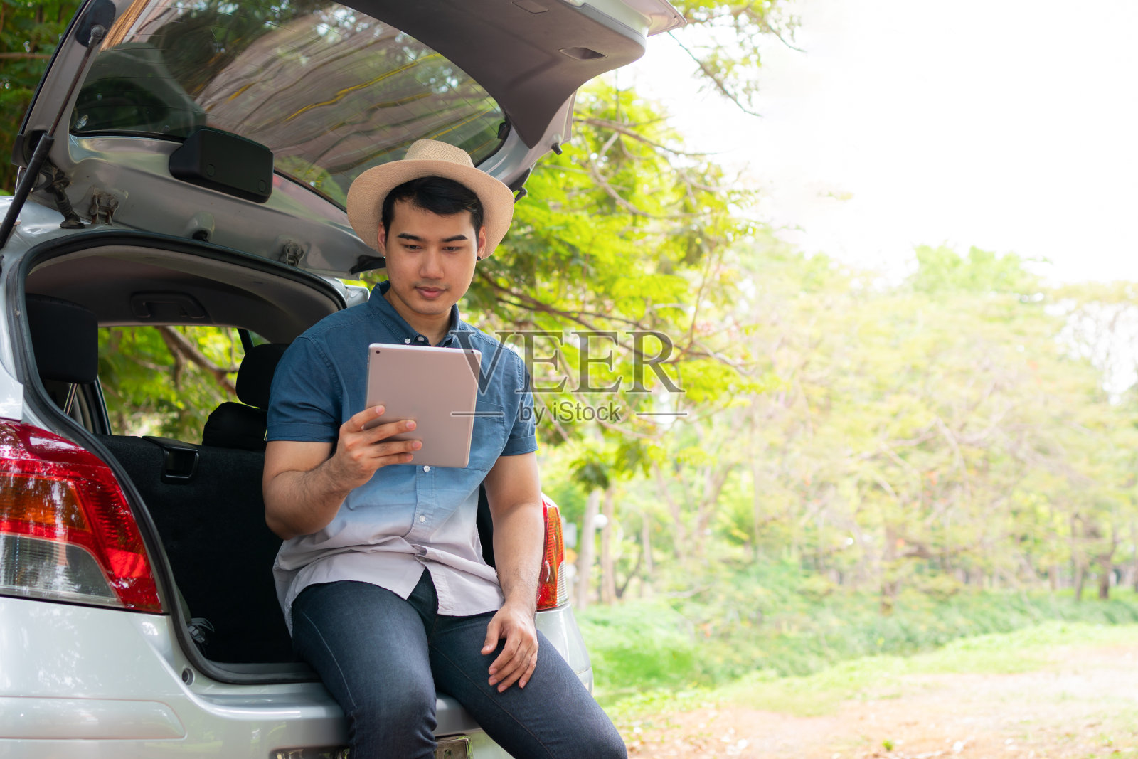 亚洲人坐在车后面，拿着桌子检查位置，找到旅行的地方。快乐的自驾游和暑假在农村。旅游休闲的概念，自驾游度假照片摄影图片