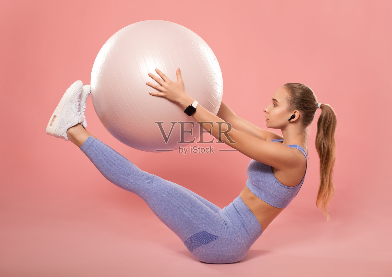 身材苗条，穿着淡紫色运动服的健美女孩，坐在垫子上拿着普拉提球，做有氧运动。运动理念，燃烧脂肪，健康生活方式。照片摄影图片