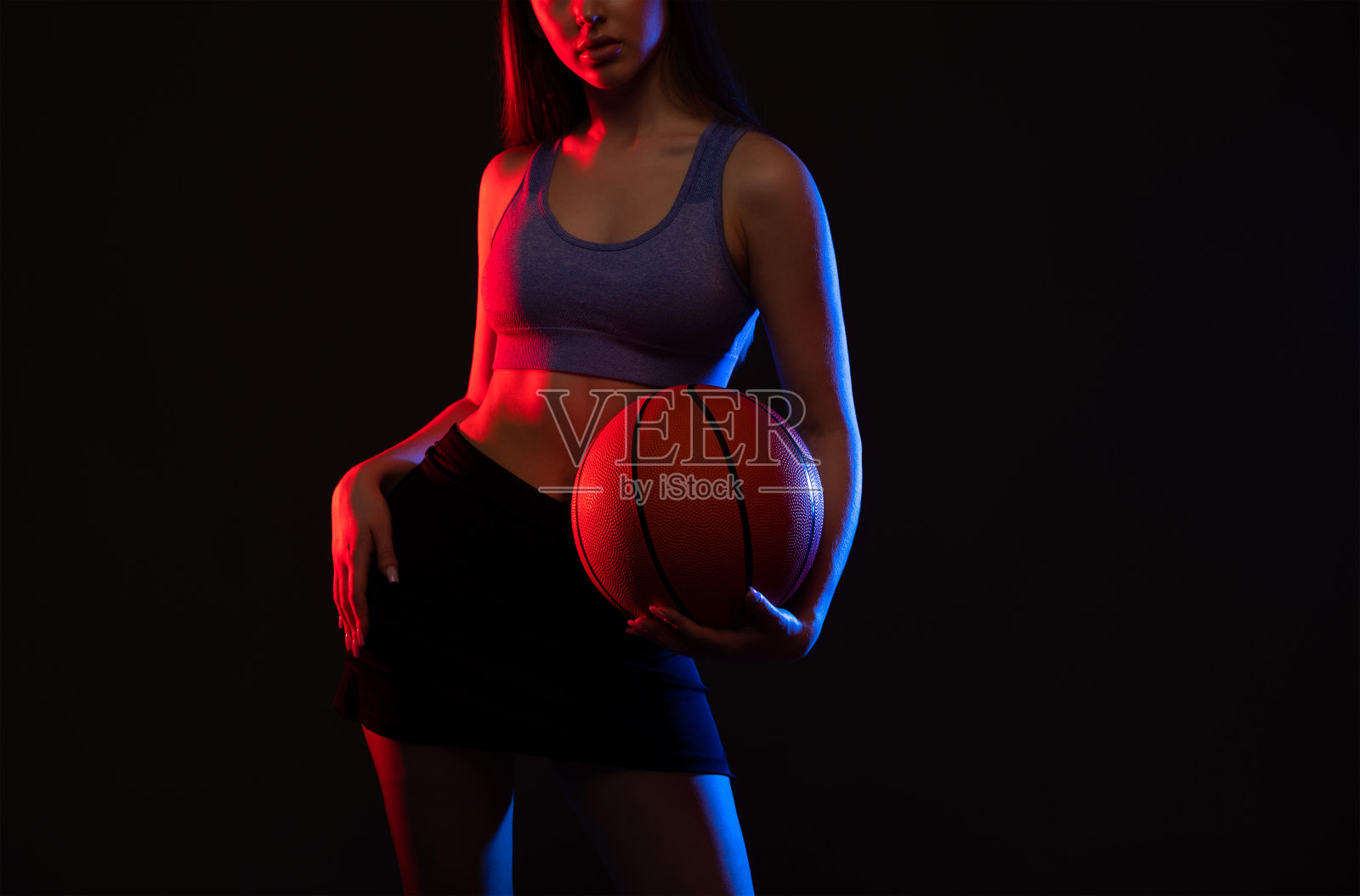 一个漂亮苗条的女孩运动员穿着短裤和上衣打篮球。照片摄影图片