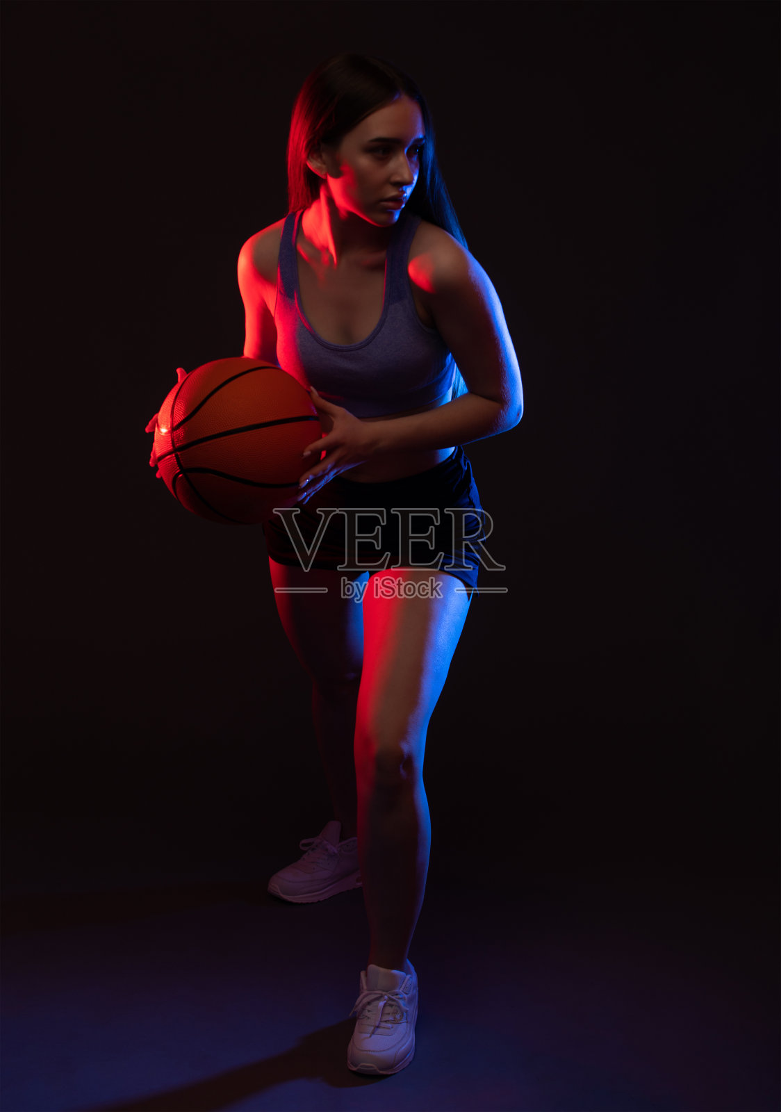 一个漂亮苗条的女孩运动员穿着短裤和上衣打篮球。照片摄影图片