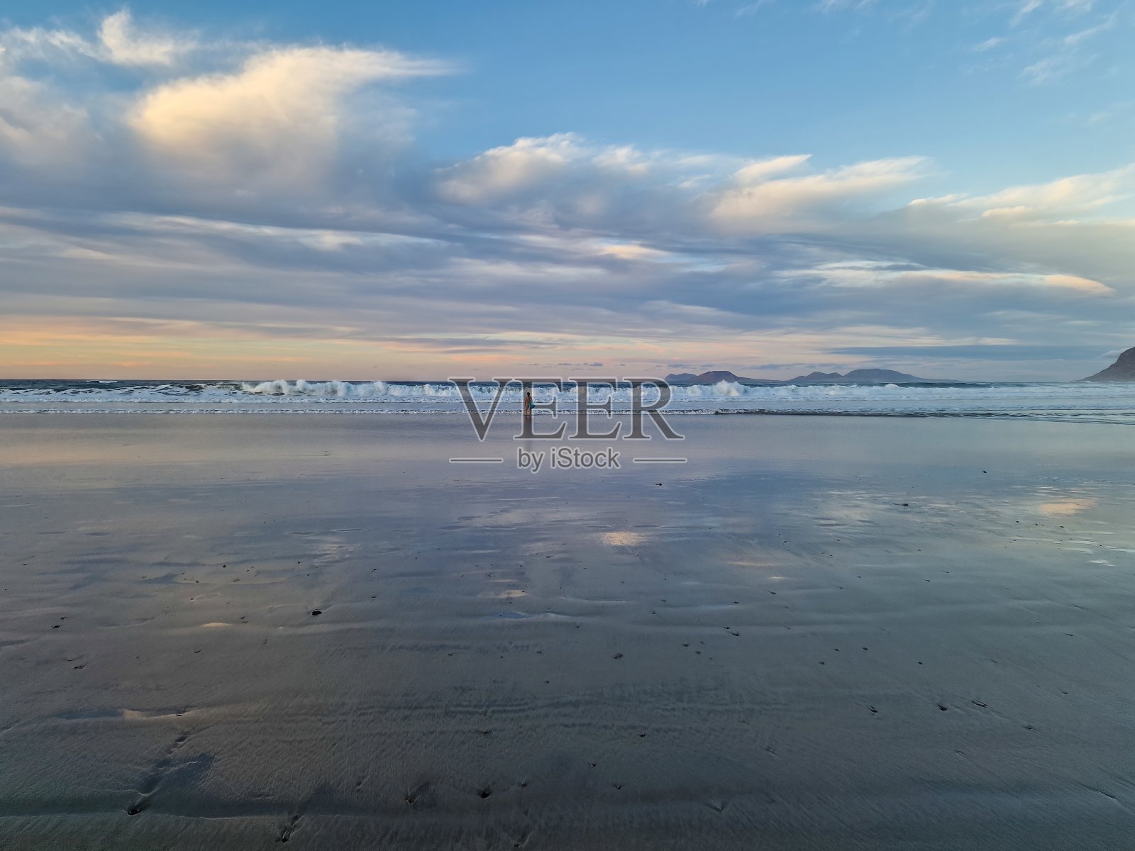 日落在法玛拉海滩，兰萨罗特岛，画了一个惊人的显示在地平线上充满活力的色彩，创造了一个迷人的场景，吸引了当地人和游客的一致照片摄影图片