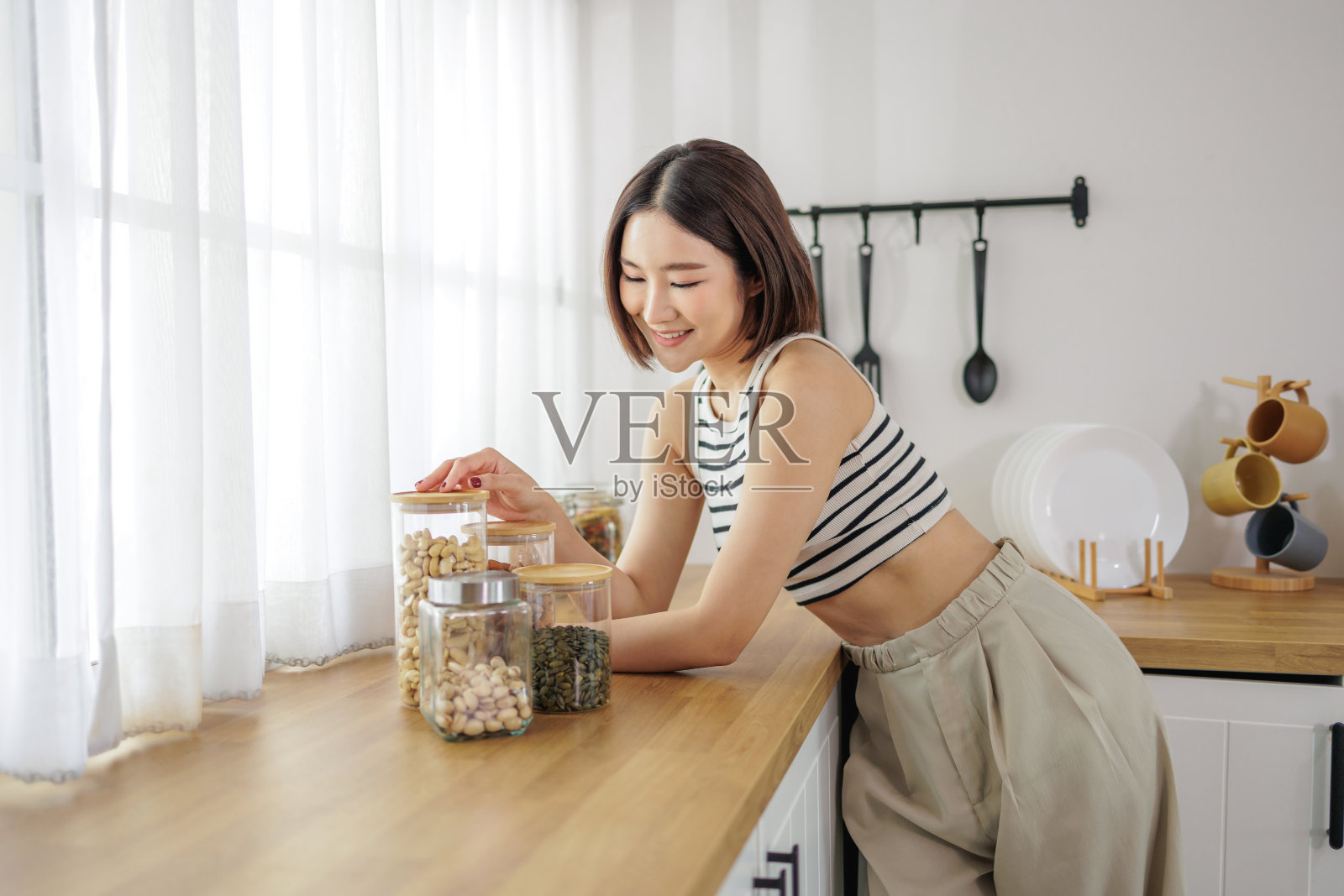 一个微笑的女人在现代厨房里整理坚果和种子的罐子，享受着做饭的乐趣照片摄影图片