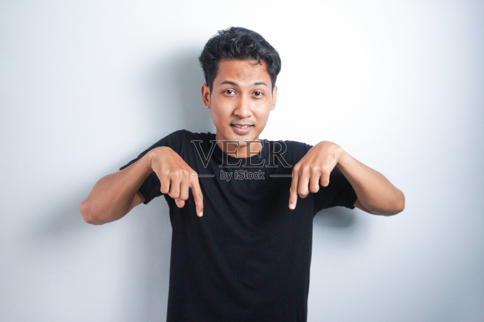 一名穿着黑色t恤的亚洲男子震惊地指着他下面被白色背景隔开的复印空间照片摄影图片