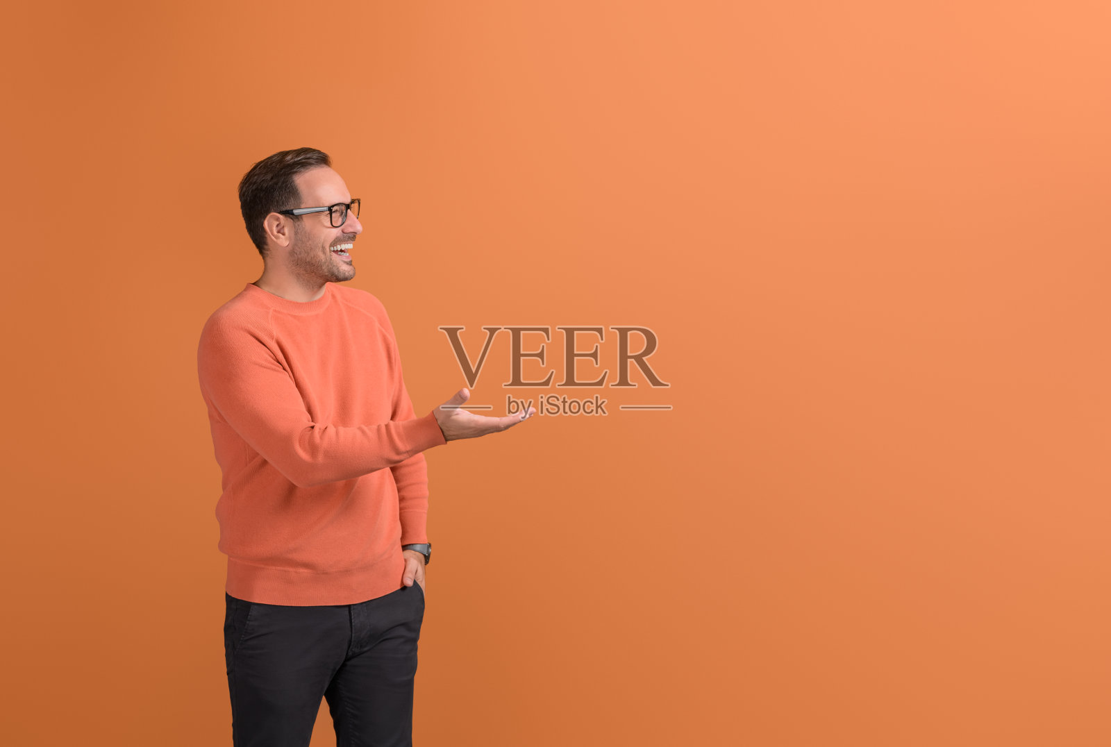 年轻的商人笑着在孤立的橙色背景上的空手掌上推销新产品照片摄影图片