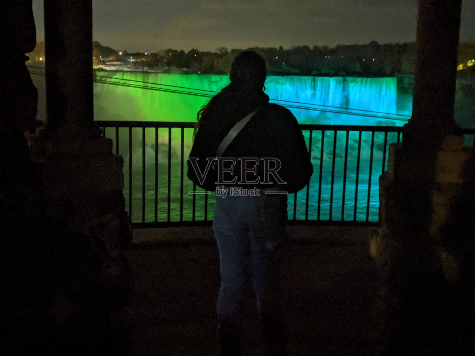 夜晚，一位妇女站在色彩斑斓的尼亚加拉大瀑布前照片摄影图片