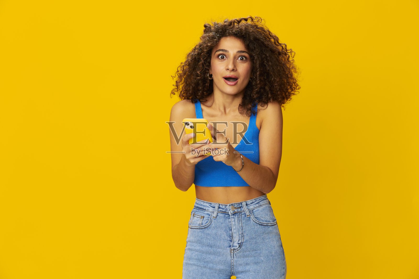 网红女人手里拿着手机自拍在视频通话中聊天自由职业者社交媒体技术工作，蓝色衬衫黄色背景的卷曲非洲头发，带着牙齿的微笑，复制空间照片摄影图片