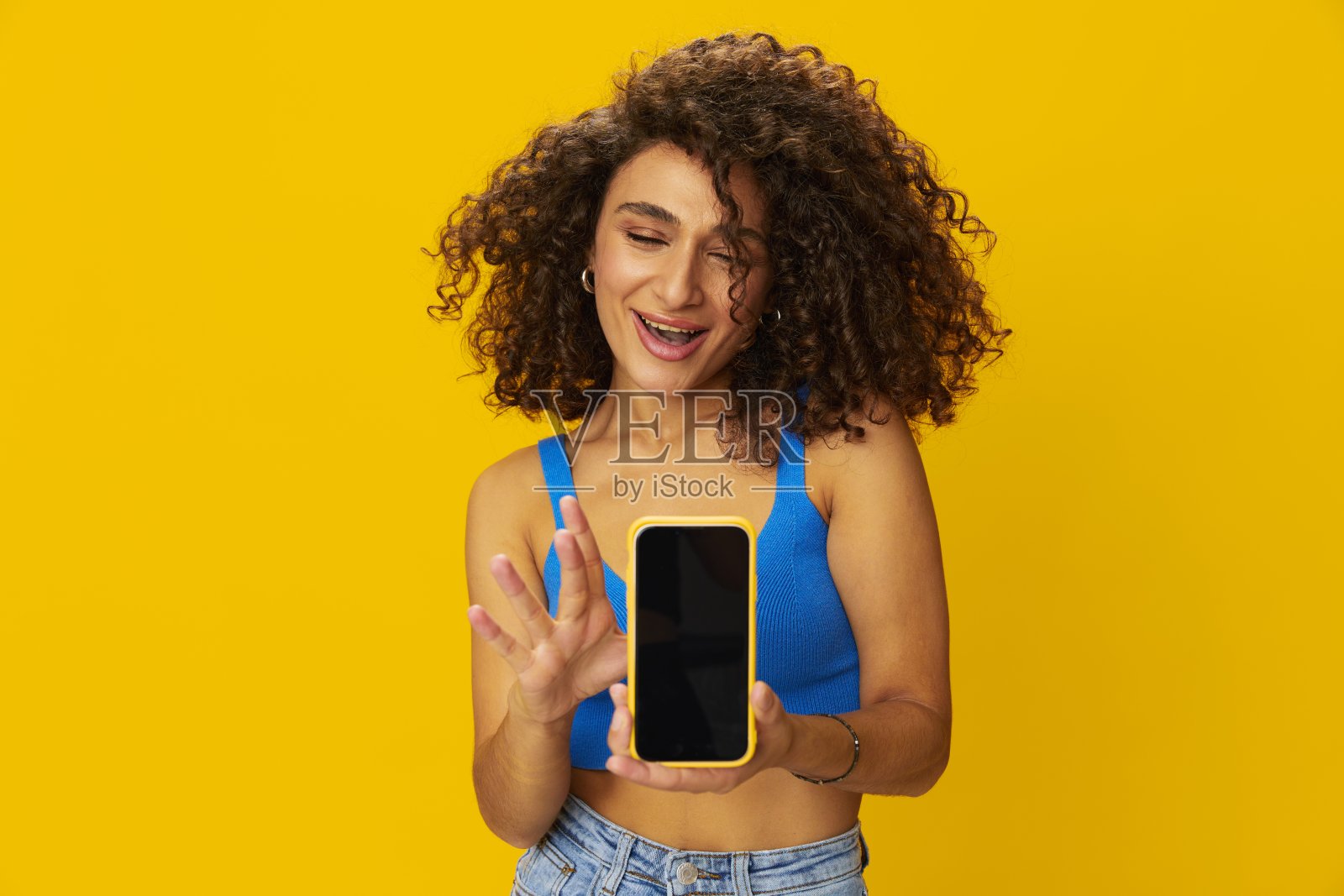 网红女人手里拿着手机自拍在视频通话中聊天自由职业者社交媒体技术工作，蓝色衬衫黄色背景的卷曲非洲头发，带着牙齿的微笑，复制空间照片摄影图片