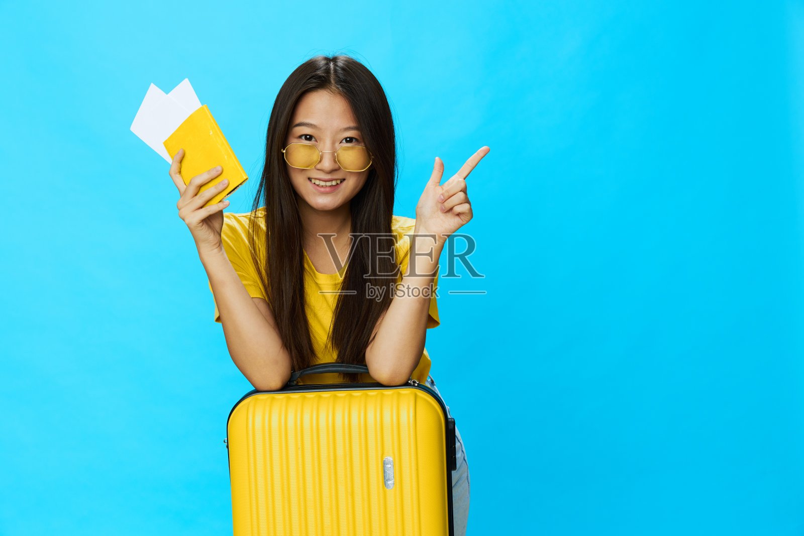 亚洲妇女带着黄色行李箱和车票，手里拿着护照，游客乘坐飞机和火车旅行，蓝色背景的行李照片摄影图片