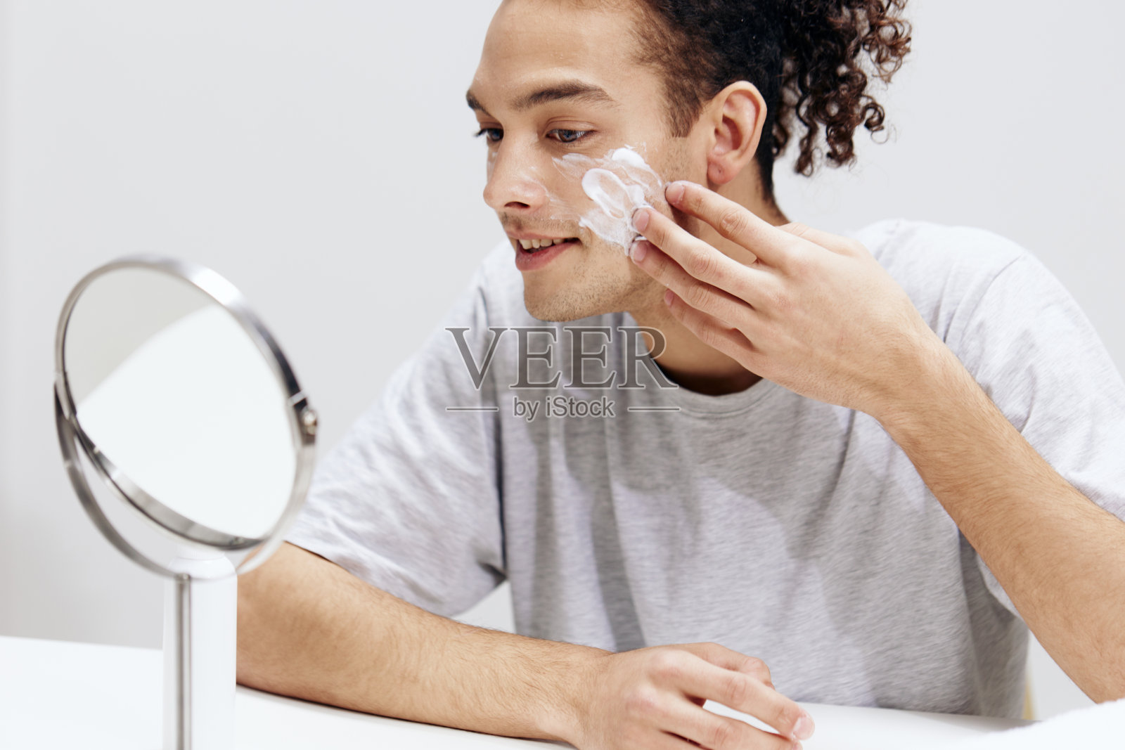 一个穿着白色t恤的男人在镜子前的皮肤护理浅背景的肖像照片摄影图片