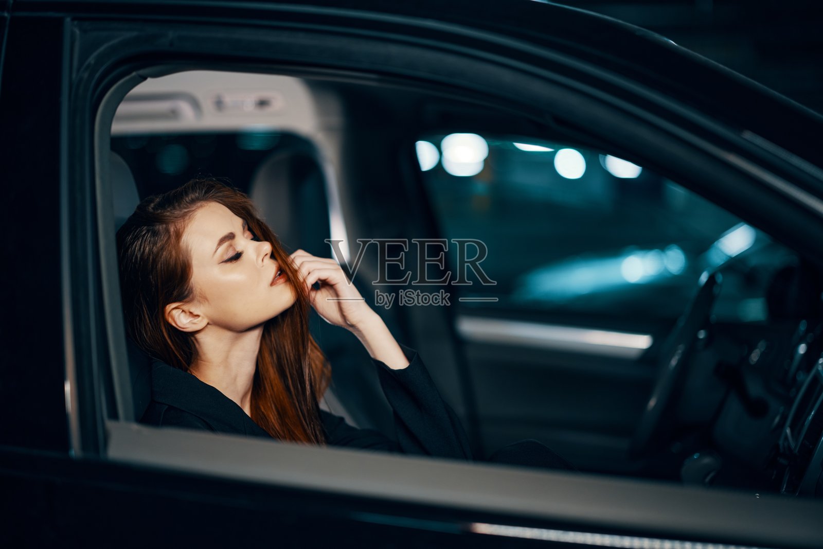 一个时髦、奢华的女人晚上坐在一辆黑色的汽车里，拉直她的长发，愉快地闭上眼睛照片摄影图片