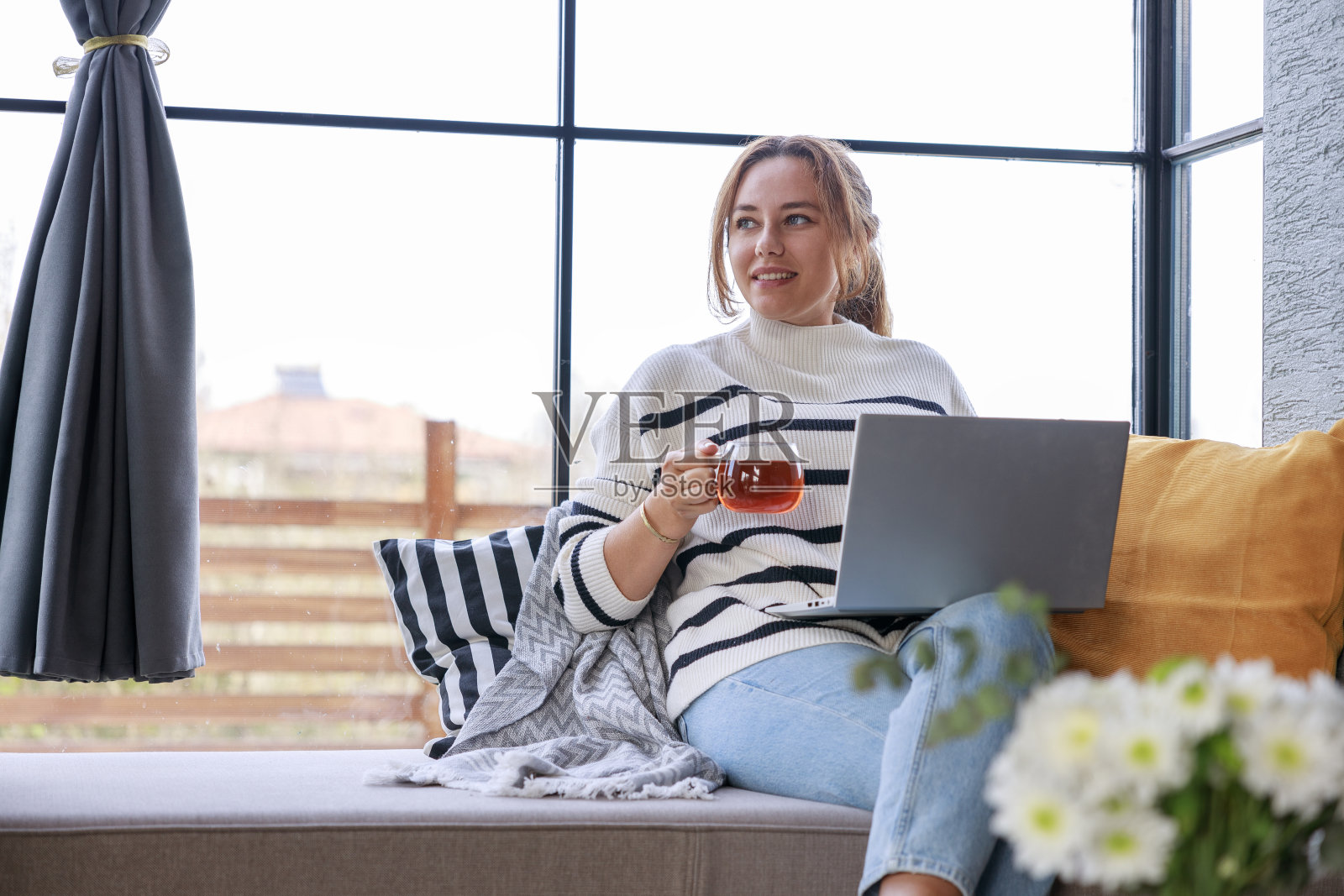 一位年轻女子在家里的窗台沙发上放松地使用笔记本电脑照片摄影图片