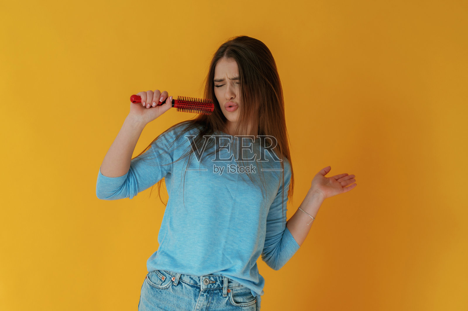 用梳子当麦克风，唱歌。黄色背景下的年轻女子照片摄影图片