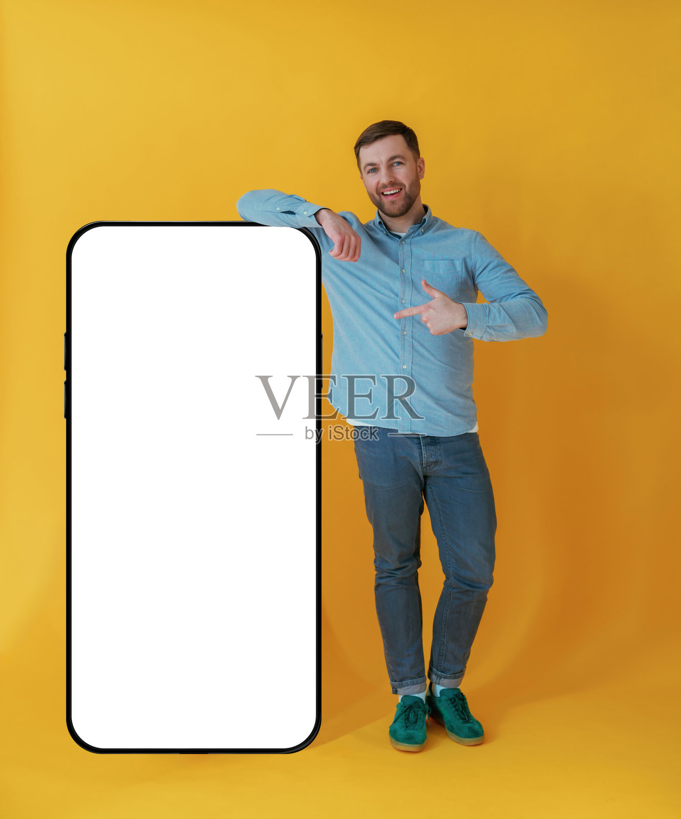 有大的智能手机复印空间。穿着蓝色衬衫的迷人男人在黄色的背景下照片摄影图片