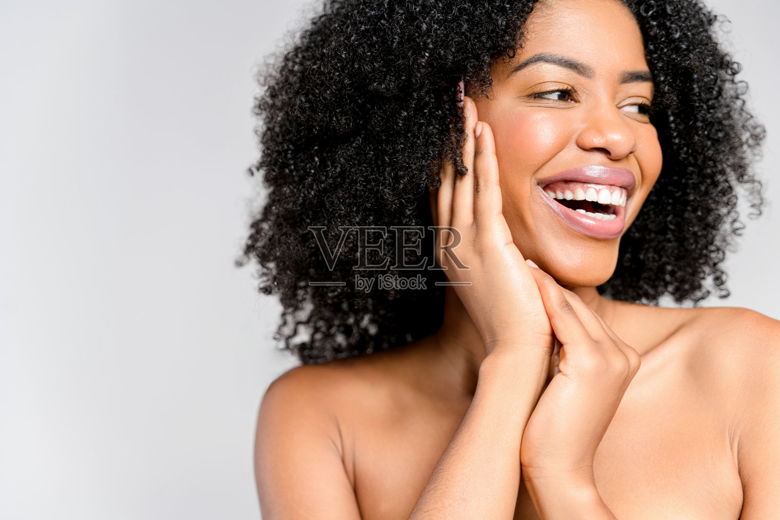 一个快乐的非洲裔美国妇女，带着活泼的微笑和自然的卷发，她的手轻轻地勾勒出她的脸照片摄影图片