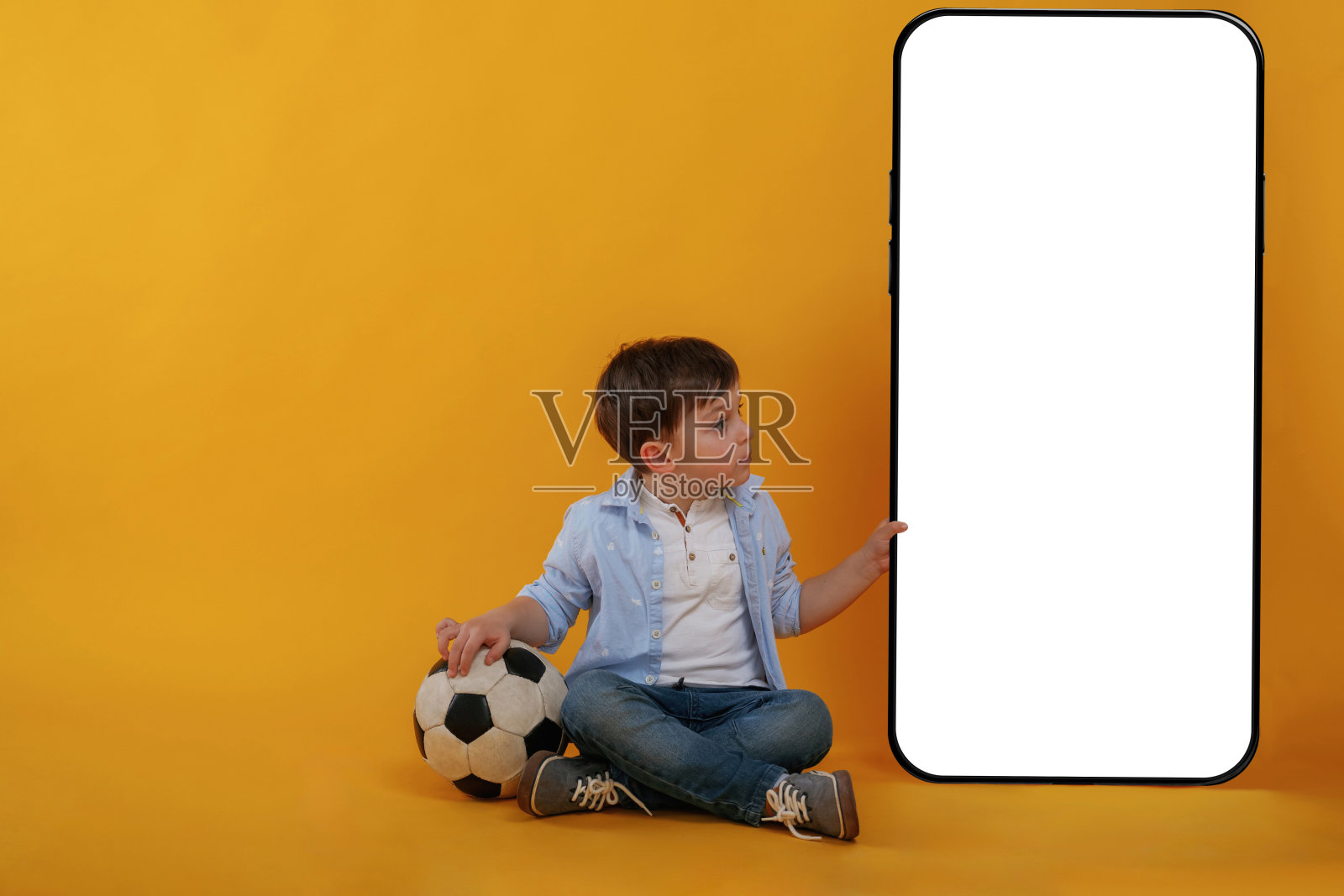 拥有巨大的智能手机，复制空间的地方。小男孩在黄色背景下的画室里照片摄影图片