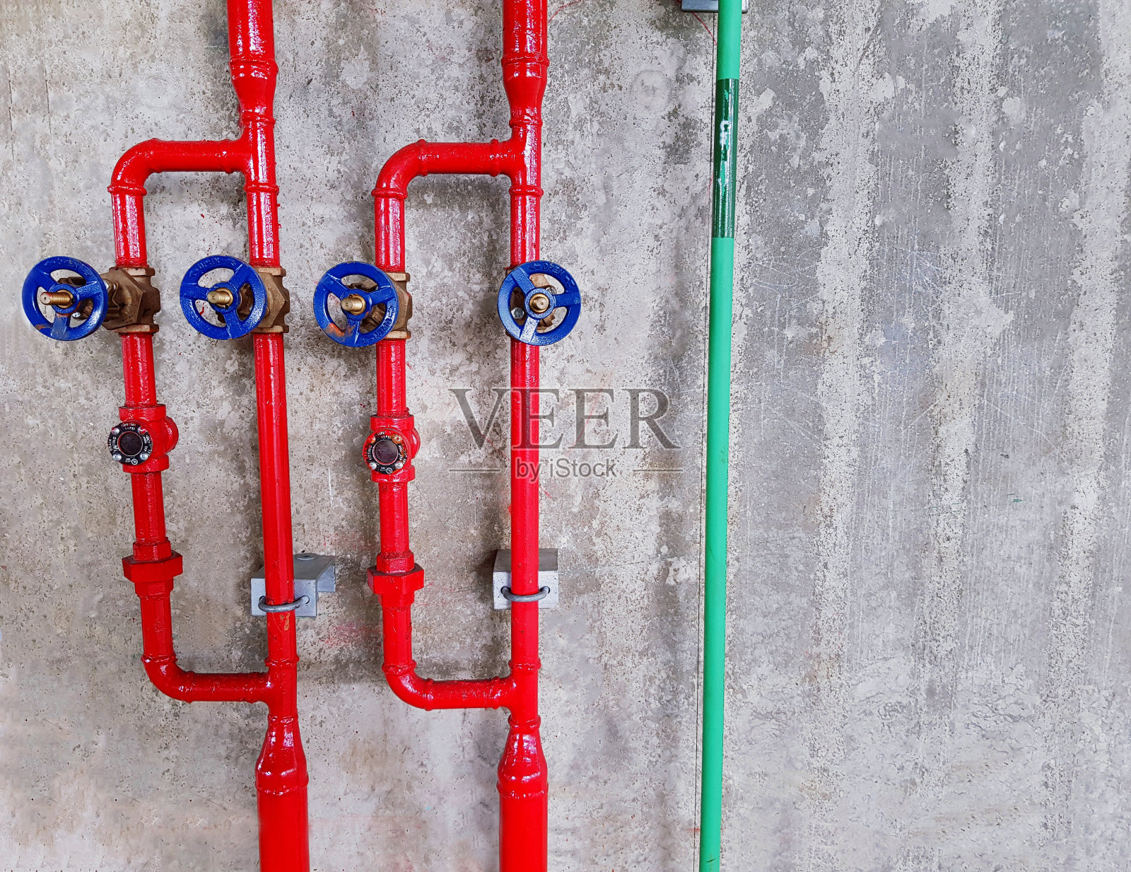 红色的水和绿色的管道与四个蓝色的水阀安装在灰色粗糙的混凝土墙背景与复制空间。工业和系统安装概念照片摄影图片
