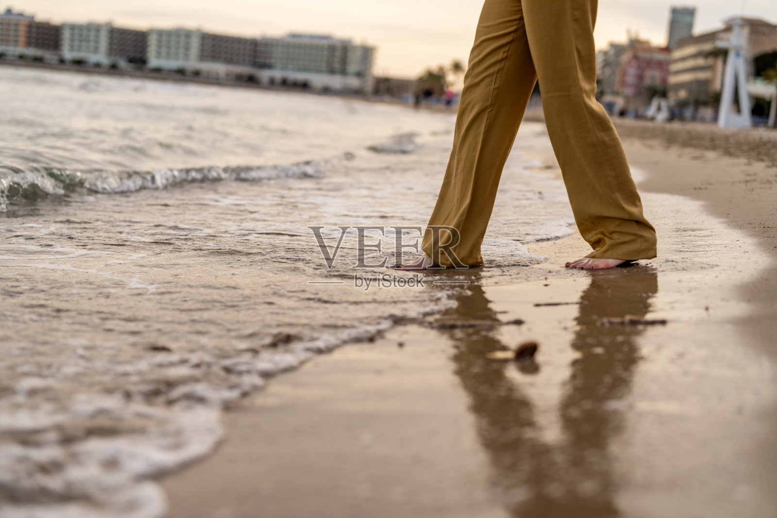 特写:年轻女子的双腿在海浪上行走。照片摄影图片