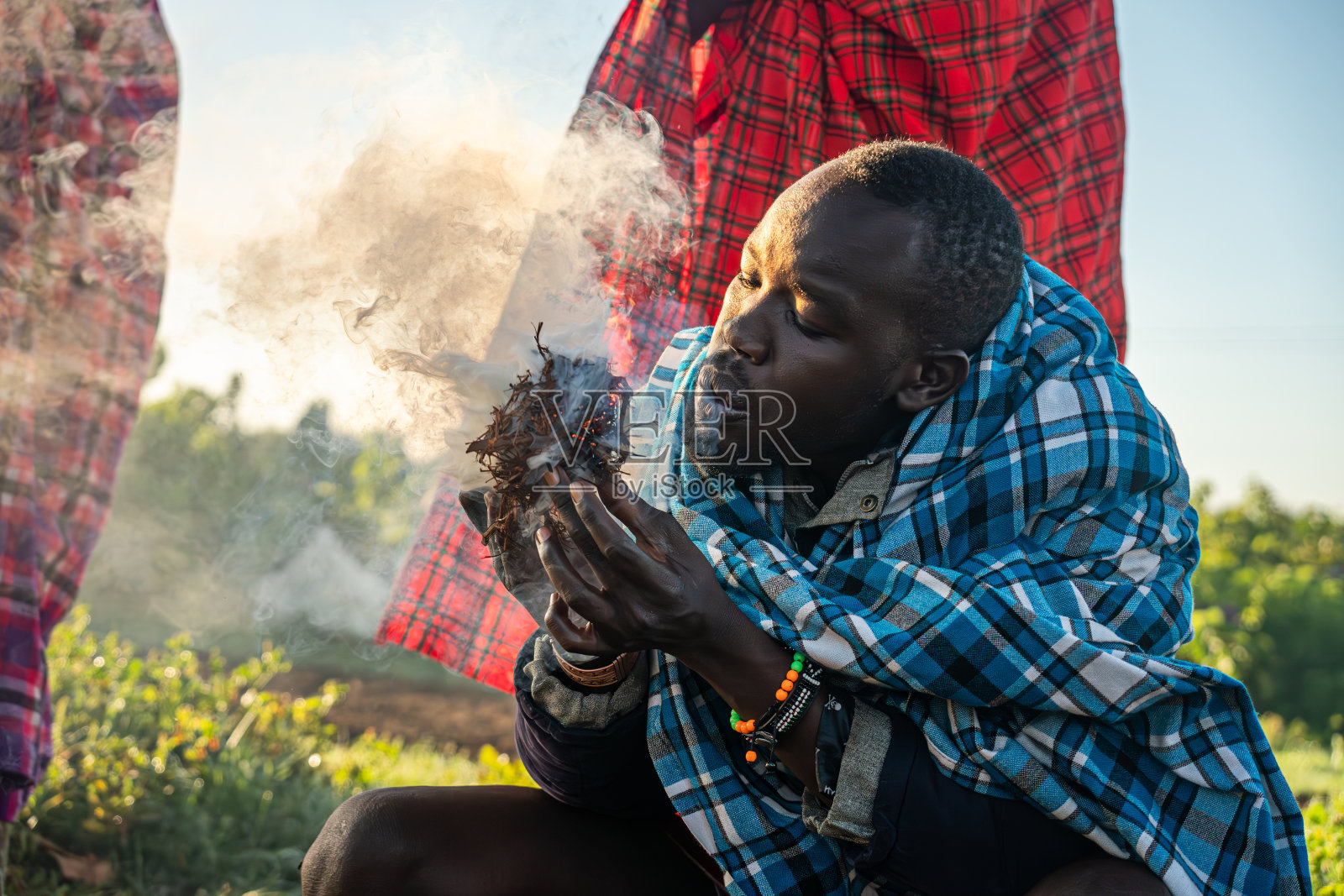 一名马赛人正在展示一种传统的点火技术，在干草着火后对着它吹气。照片摄影图片
