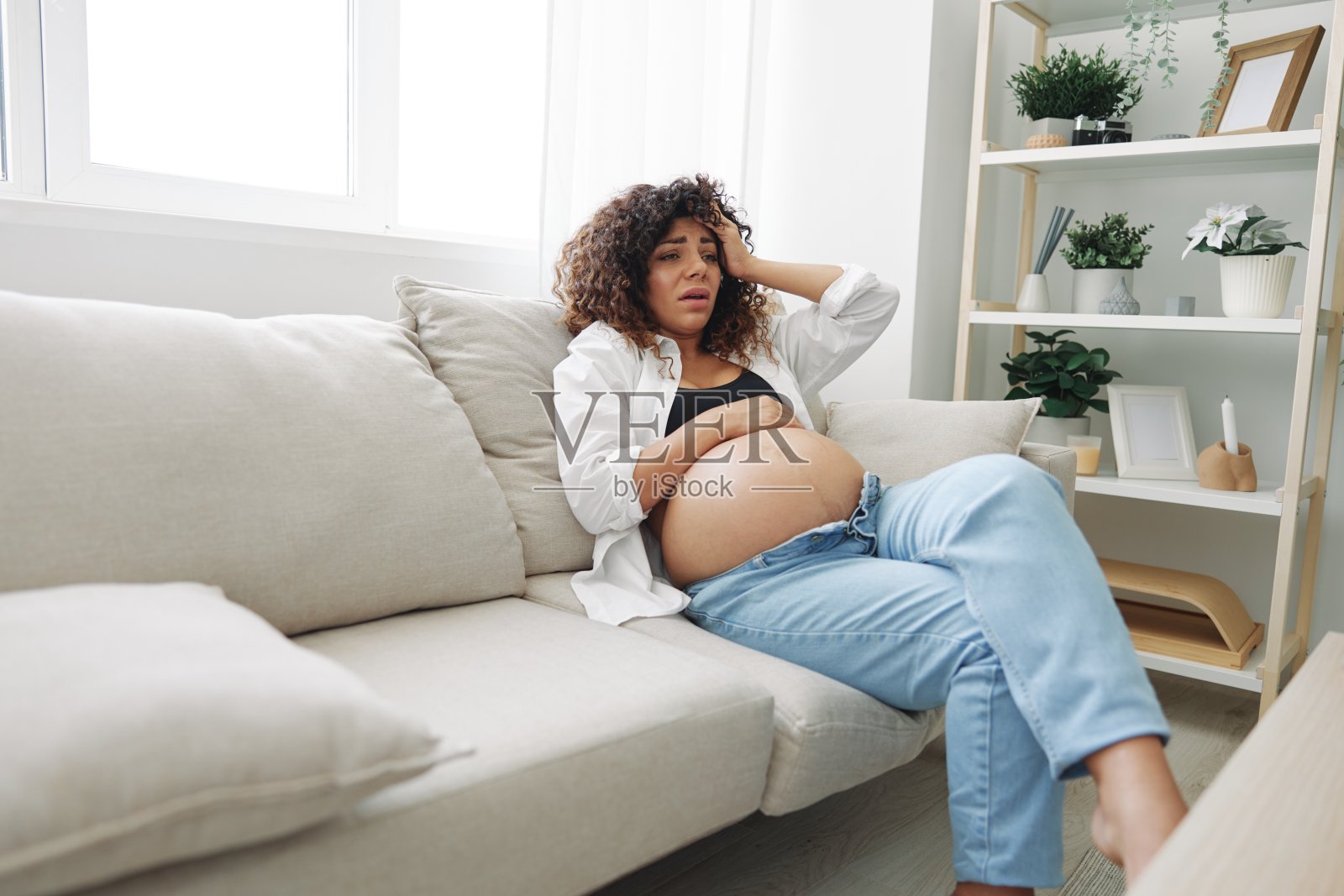孕妇头痛躺在家里的衬衫和牛仔裤沙发上疲劳和沉重在怀孕前的最后一个月，生活方式困难的母亲，恶心照片摄影图片