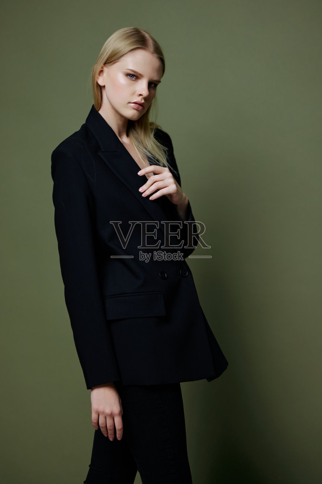 一个有吸引力的酷职业模特拿着一件夹克的翻领，在绿橄榄色的背景下在工作室里摆姿势。酷炫的品牌横幅照片摄影图片