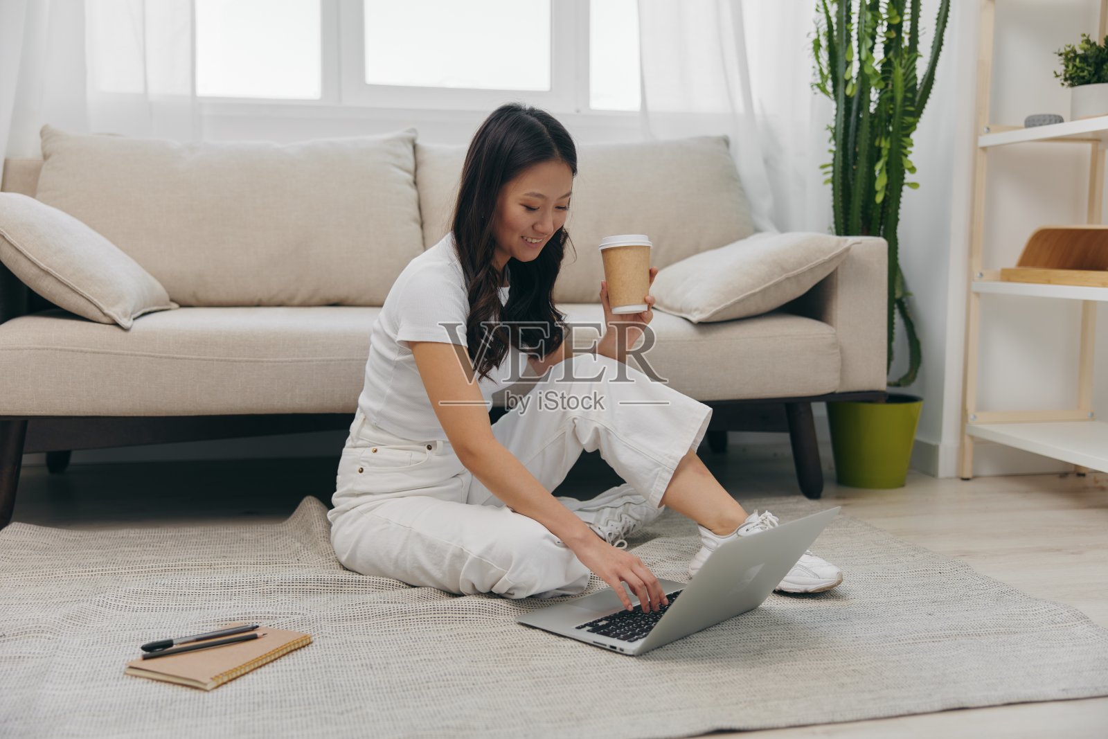 年轻的亚洲女学生看着笔记本电脑屏幕坐在家里的地板上用笔记本写字，生活方式自由职业者照片摄影图片
