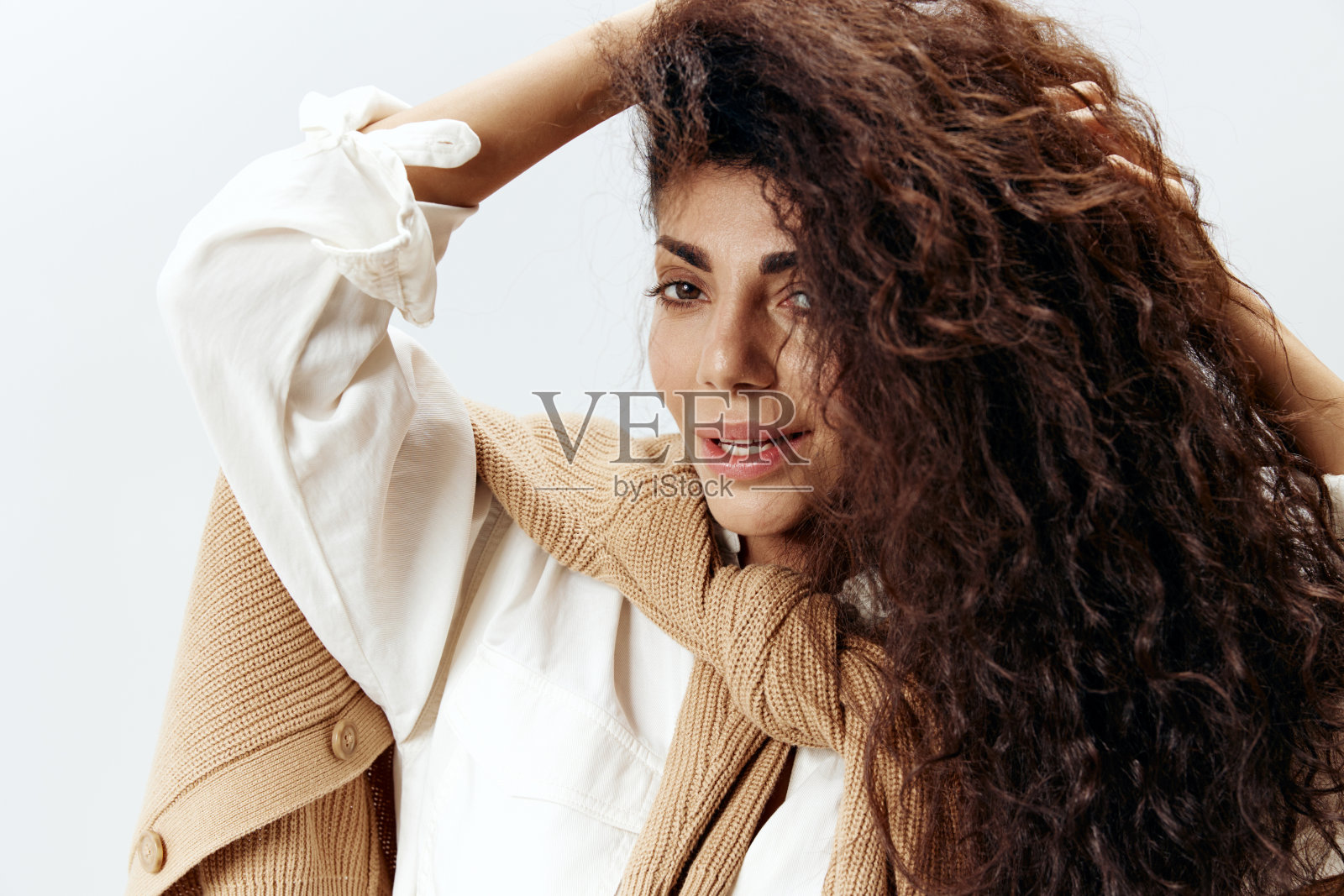 近距离肖像卷曲漂亮的拉丁女性在柔和的温暖的毛衣和白衬衫触摸干燥的头发在白色的工作室墙背景摆孤立。时尚季节性销售新系列概念。照片摄影图片