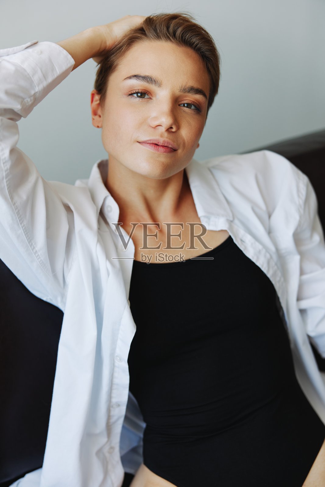 女人躺在家里沙发上的画像，剪着短发穿着白衬衫，微笑着，忧郁的少年，回家度假照片摄影图片