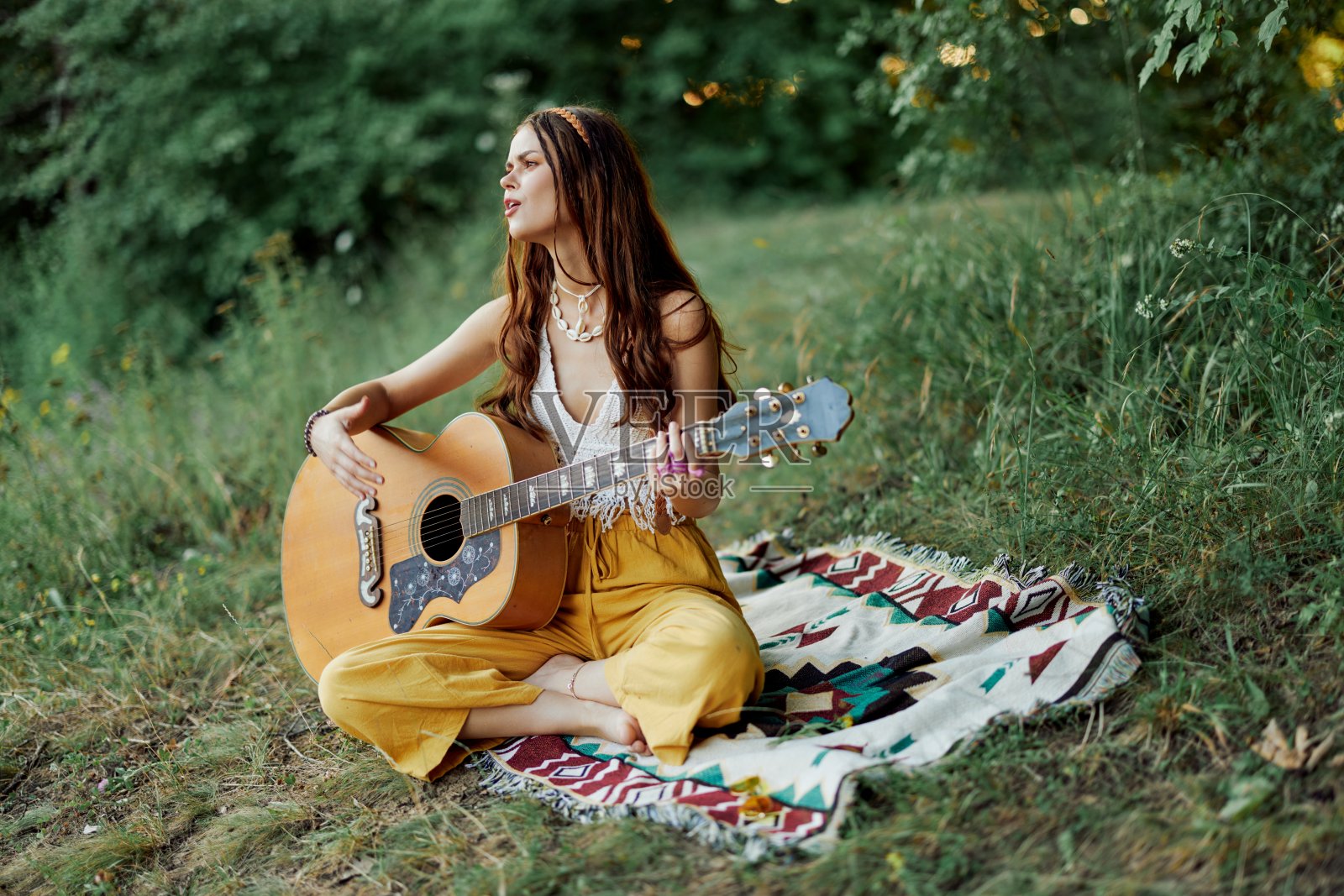 年轻的嬉皮女艺术家在秋天，穿着环保的衣服坐在大自然外面的地上，一边弹吉他一边唱歌，看着窗外的日落照片摄影图片