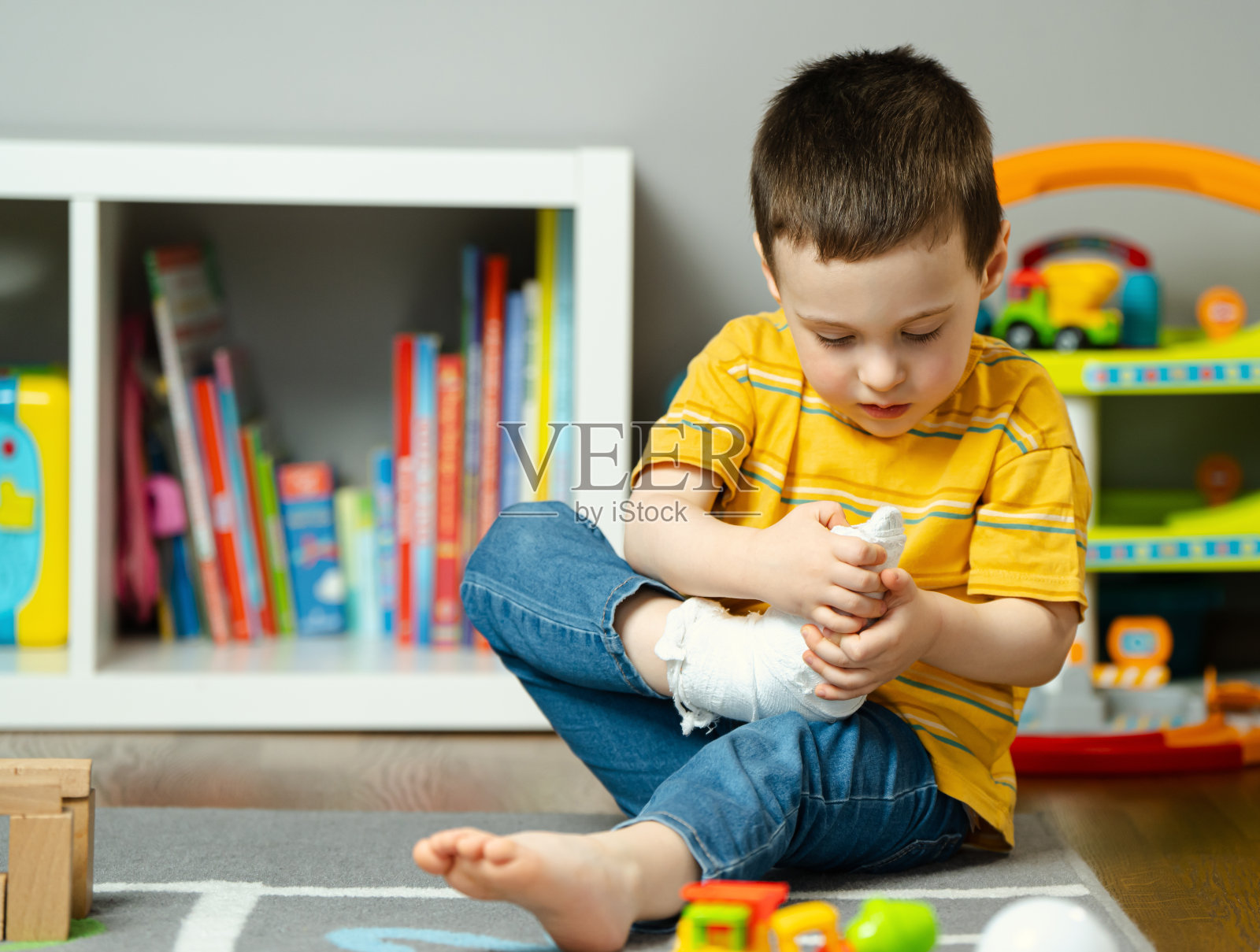 一个蹒跚学步的小男孩用手托着打了石膏的腿。儿童足部及手指骨折。人类医疗保健和医学理念。绷带照片摄影图片