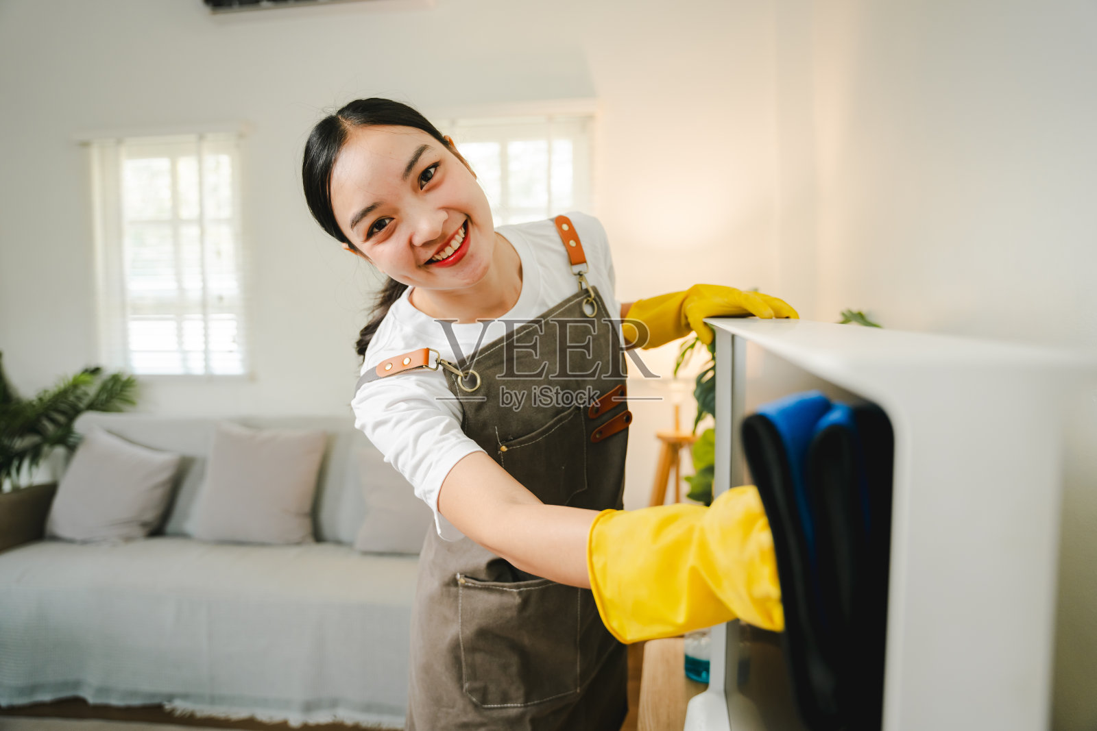 一位年轻的家庭主妇正在客厅用超细纤维布擦拭电视机上的灰尘。管理的概念照片摄影图片