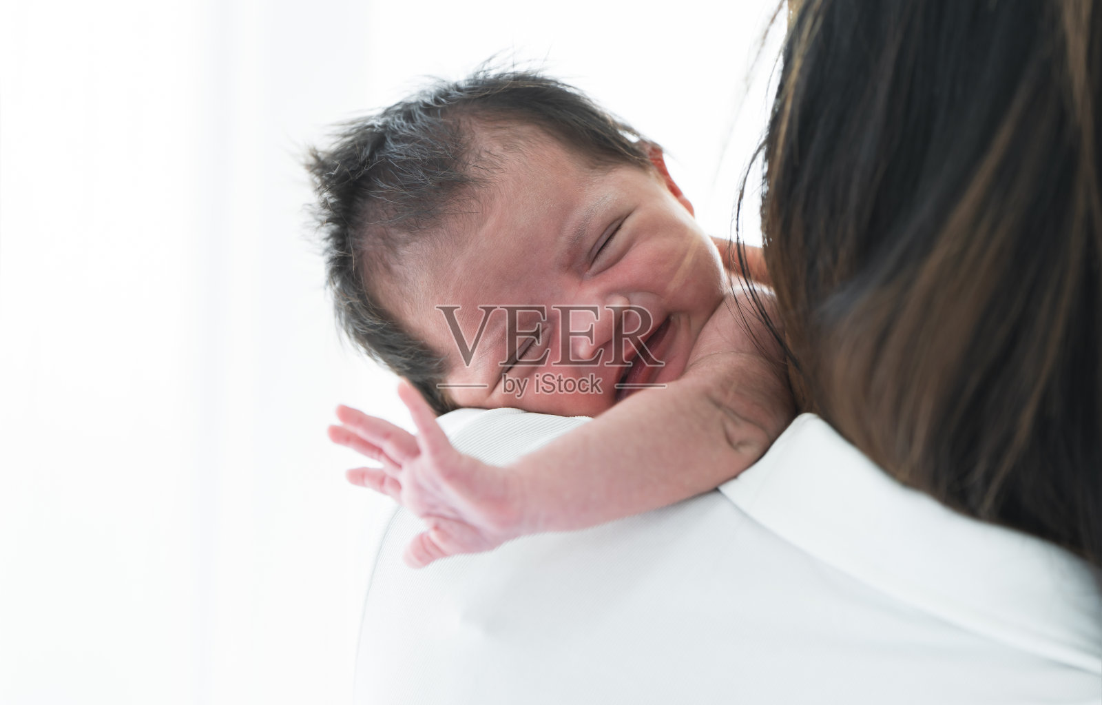 母亲在家里把刚出生的女婴背在肩上。可爱的19天亚洲澳大利亚婴儿婴儿微笑，睡在妈妈怀里快乐。父母和孩子一起放松照片摄影图片