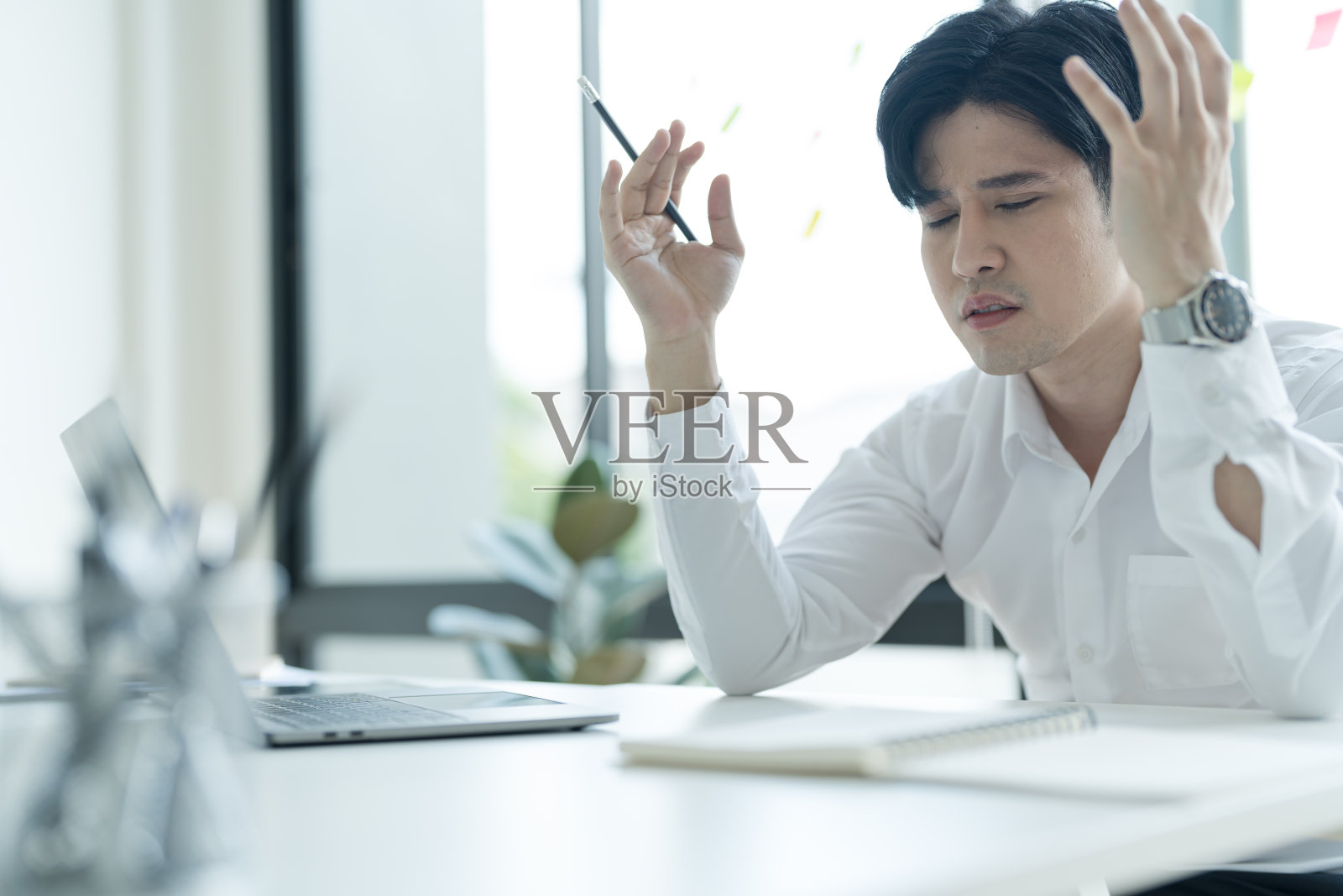 年轻的商人坐在办公桌前用笔记本电脑上网，感觉压力很大。照片摄影图片