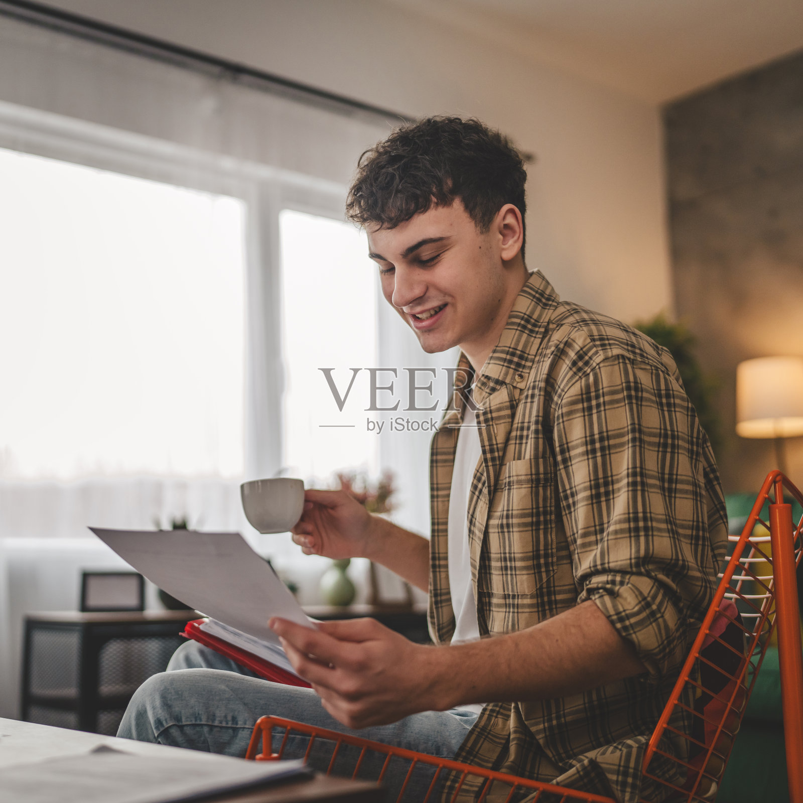 年轻人拿着纸在信里读好消息坐在家里收到信件银行对账单或通知邀请奖学金喜讯或考试报告照片摄影图片