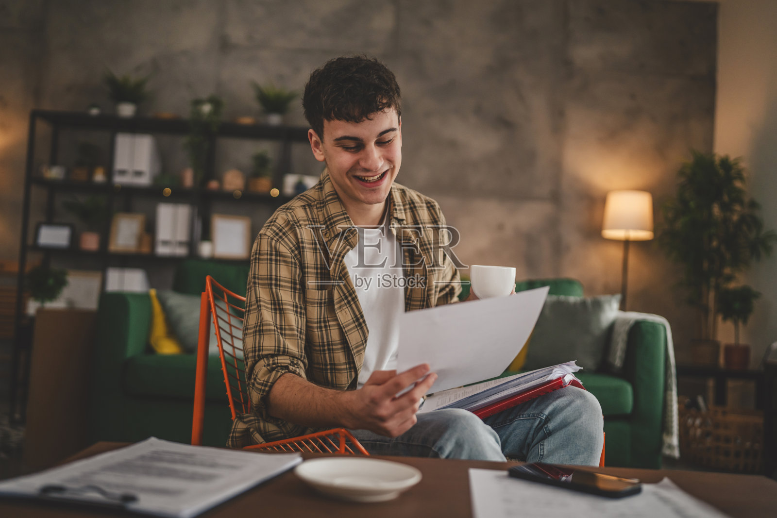 年轻人拿着纸在信里读好消息坐在家里收到信件银行对账单或通知邀请奖学金喜讯或考试报告照片摄影图片