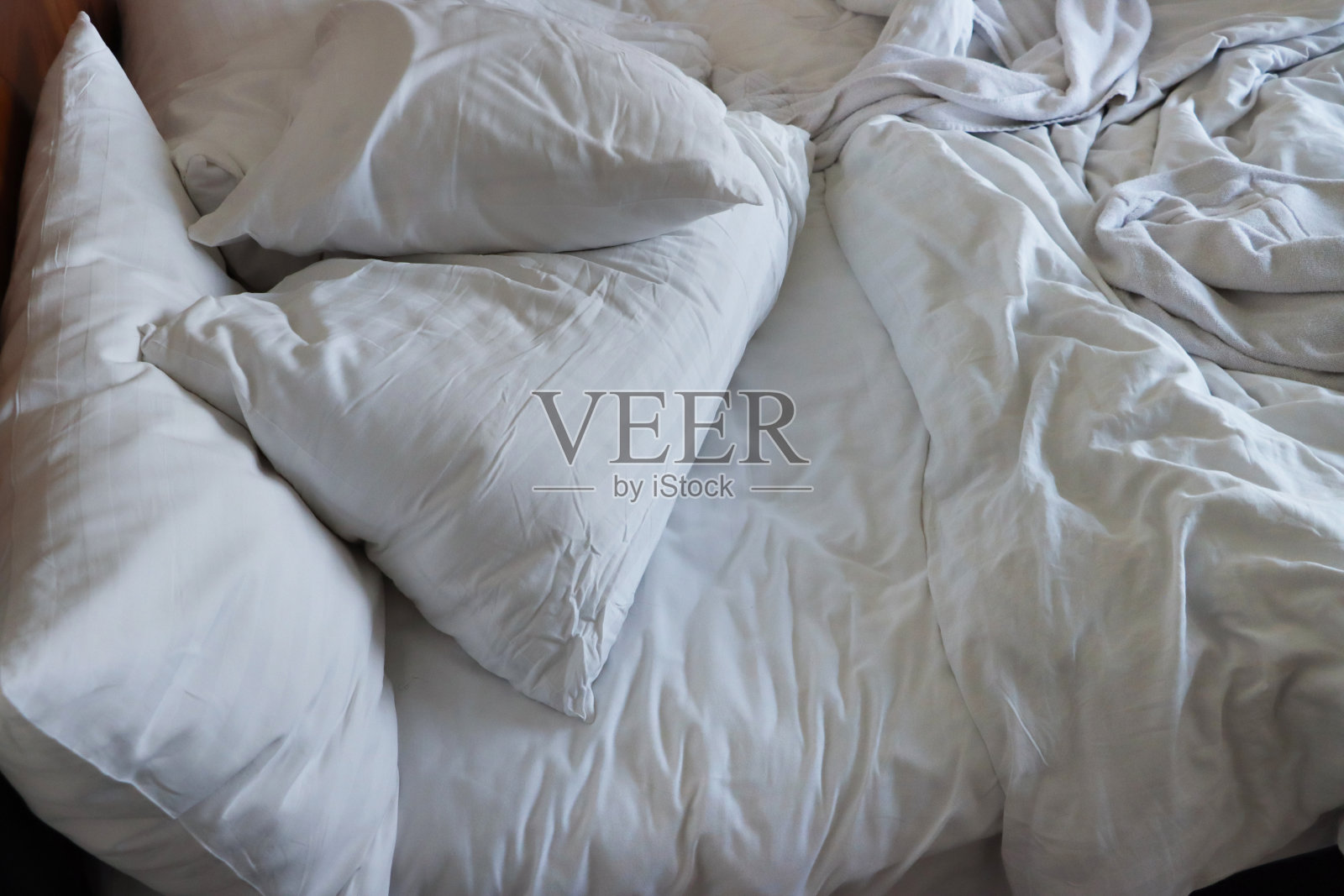 酒店卧室里凌乱的双人床、皱巴巴的床单、皱巴巴的枕头和羽绒被，全景图照片摄影图片