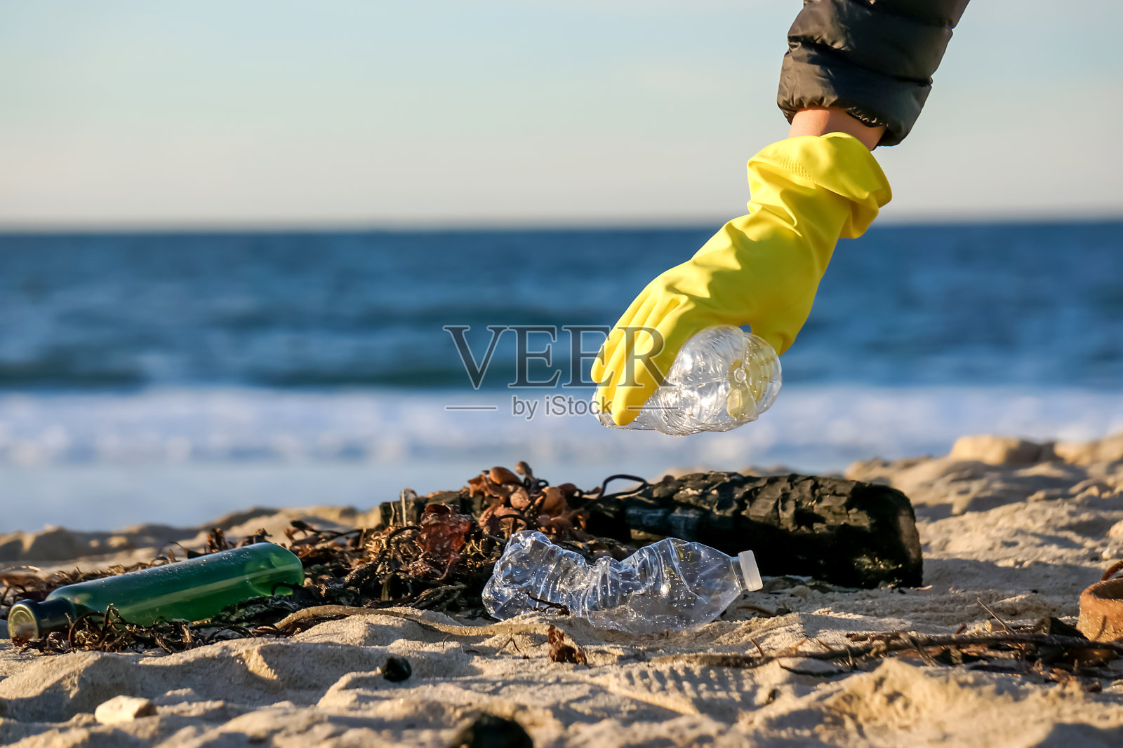 戴手套的人在沙滩上捡塑料瓶照片摄影图片