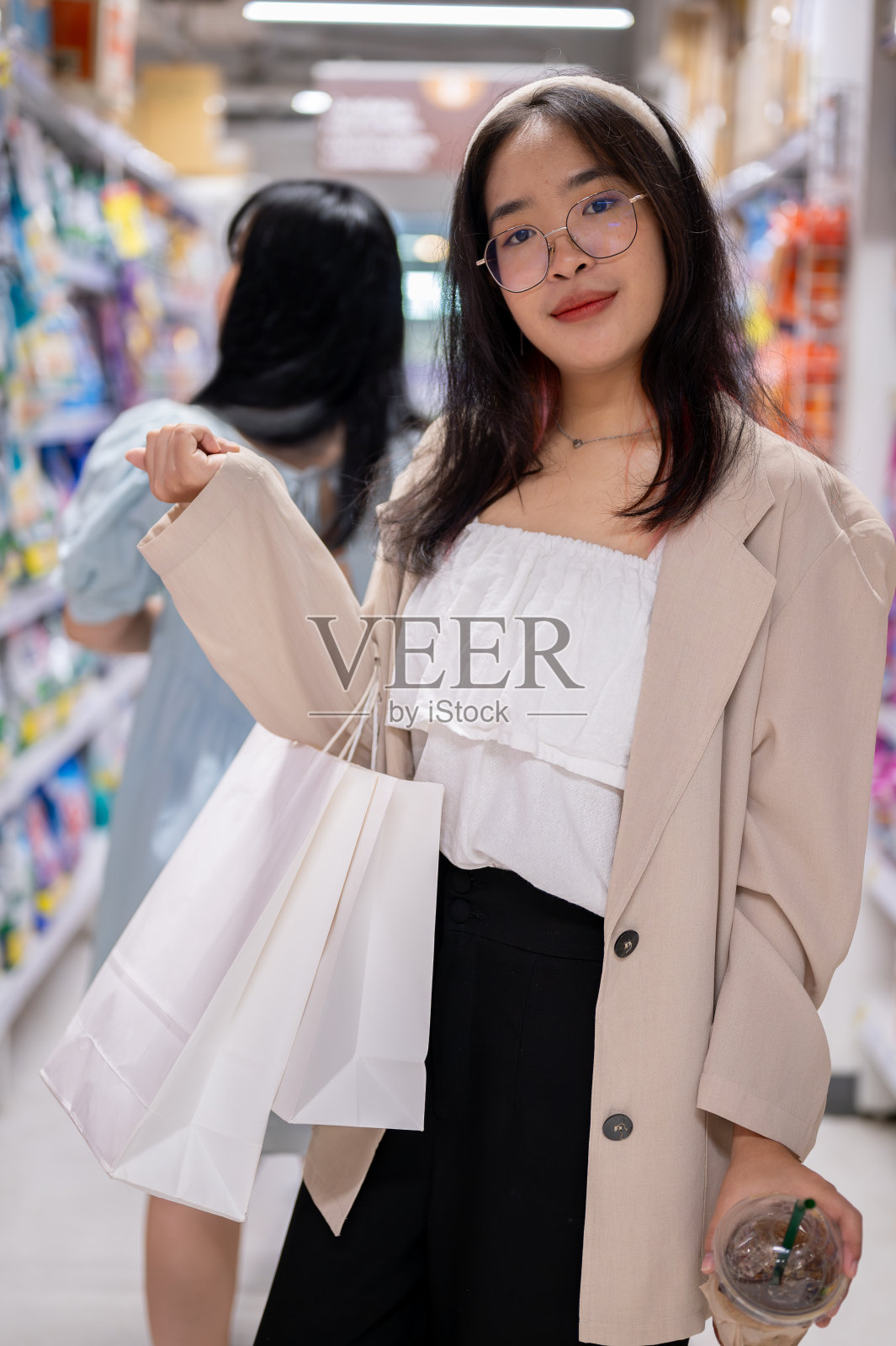 一位面带微笑的亚洲妇女站在杂货店的过道里，拿着购物袋，在超市购物。照片摄影图片